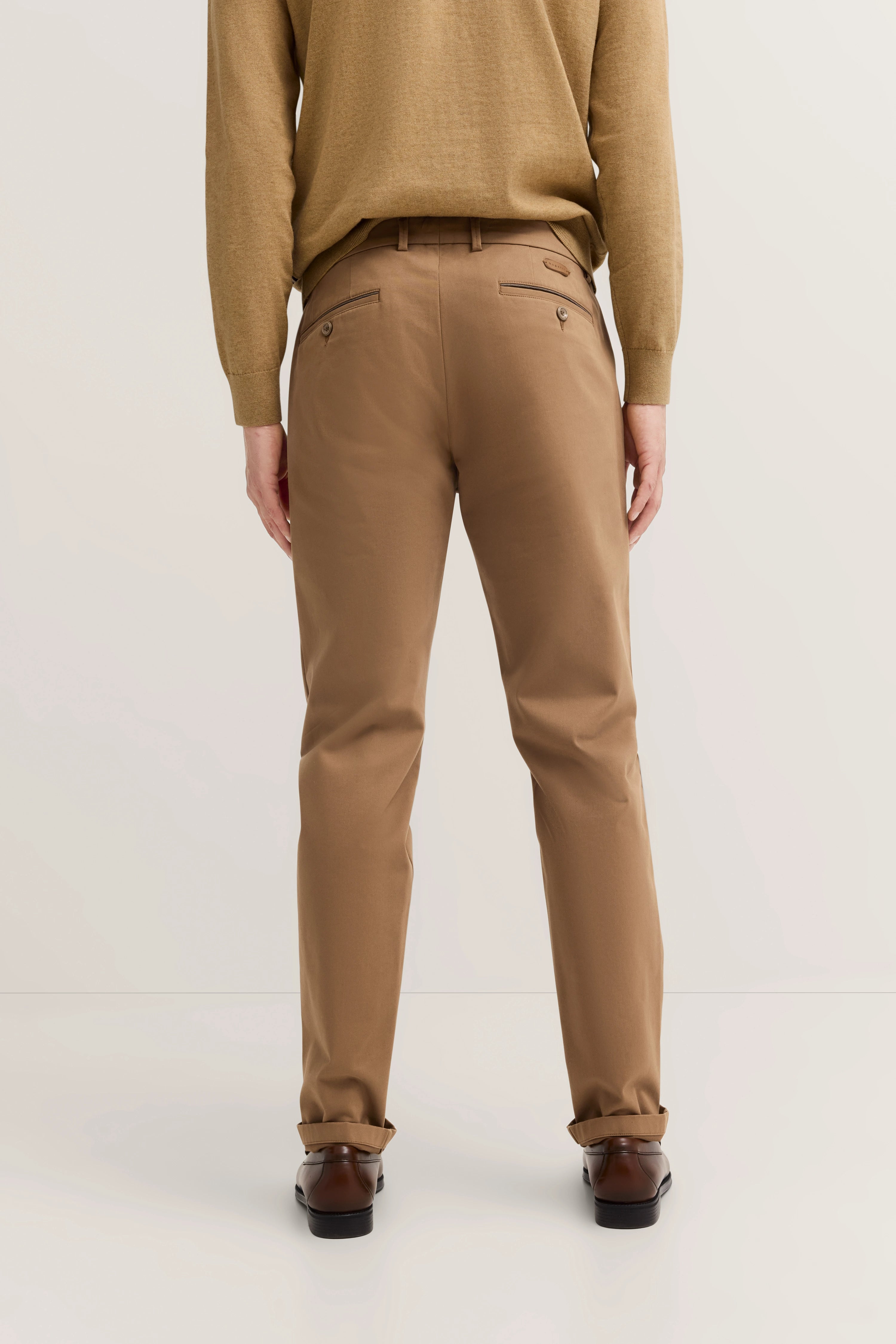 bugatti Modelbild: Beige Chino, brauner Pullover, braune Schuhe. Rückansicht, entspanntes Posing.
