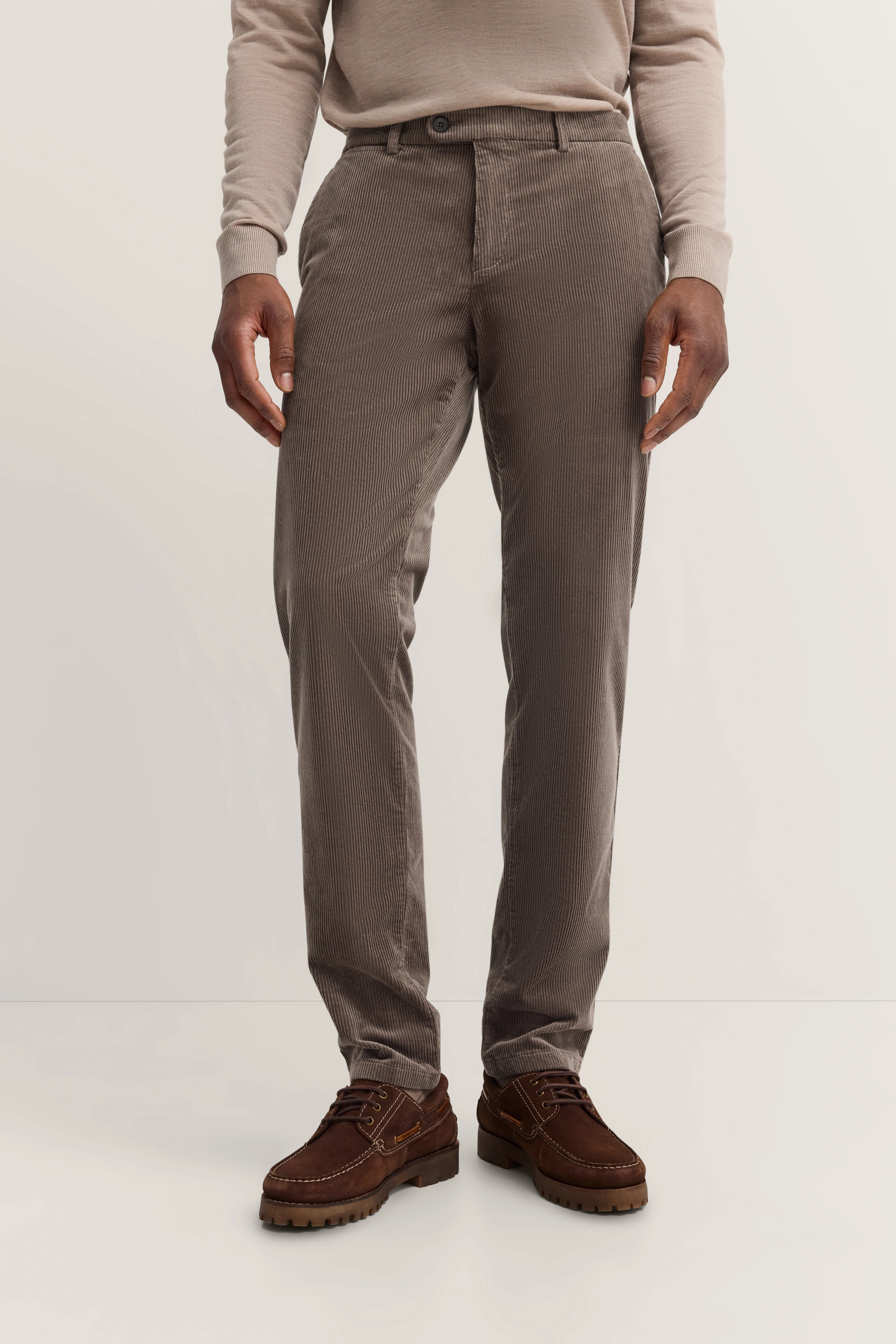 Brown corduroy trousers and sweater, casual model pose, relaxed demeanor.
