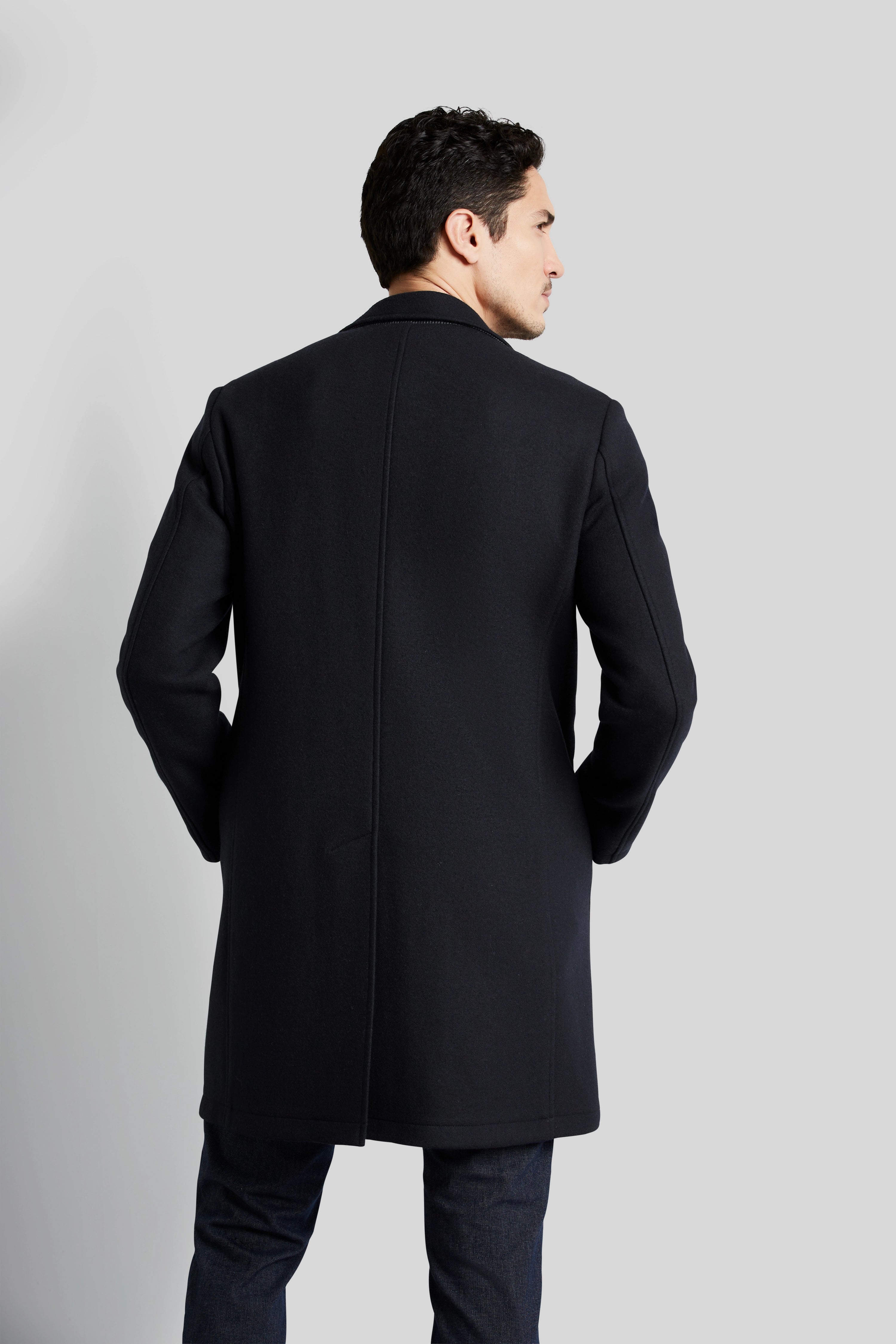 Schwarzer bugatti Mantel, Rückansicht, getragen von Model, entspannte Pose, kombiniert mit dunkler Jeans.