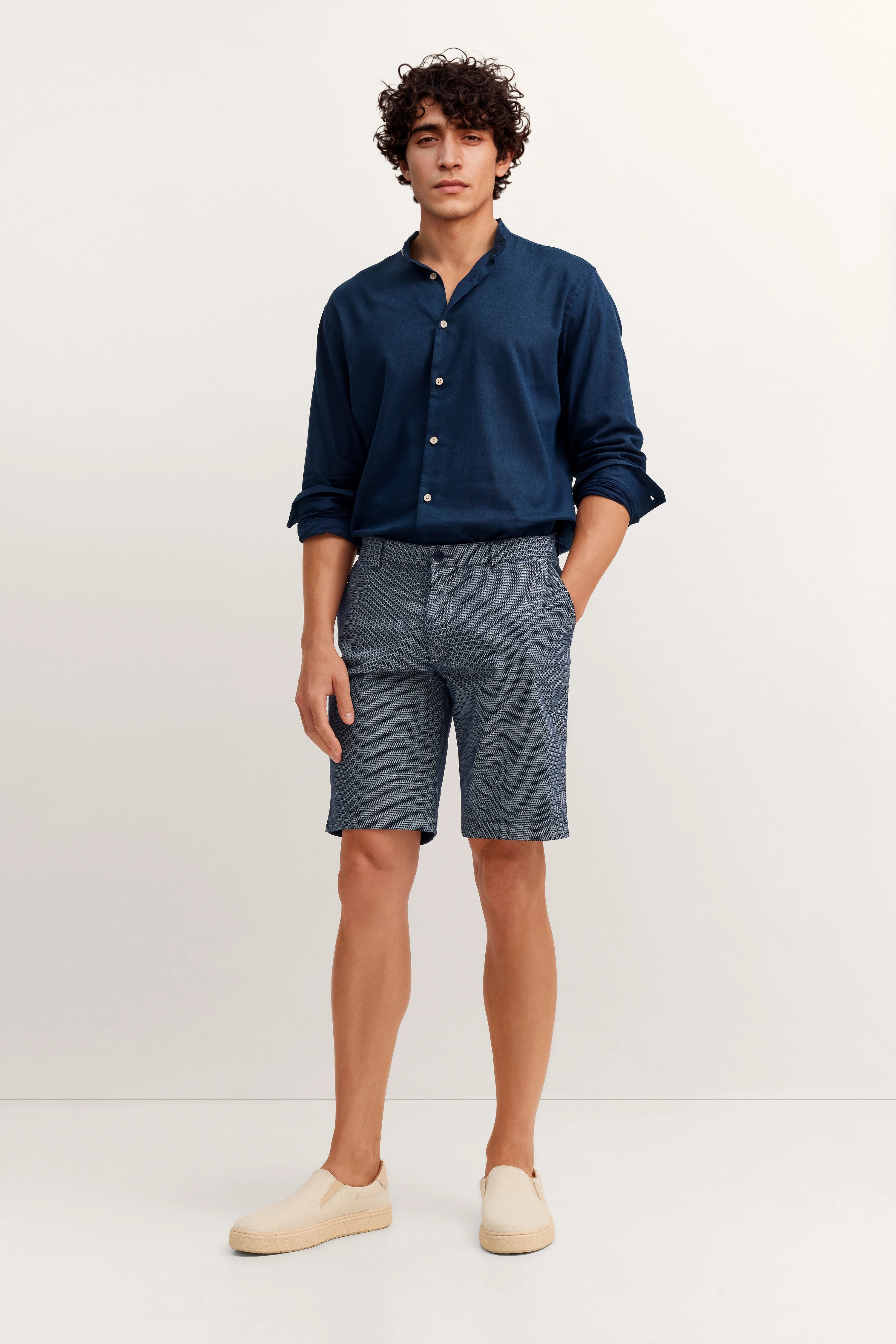 Model in blauem Hemd und gemusterten Shorts von bugatti, legeres Posing, helle Slip-Ons.