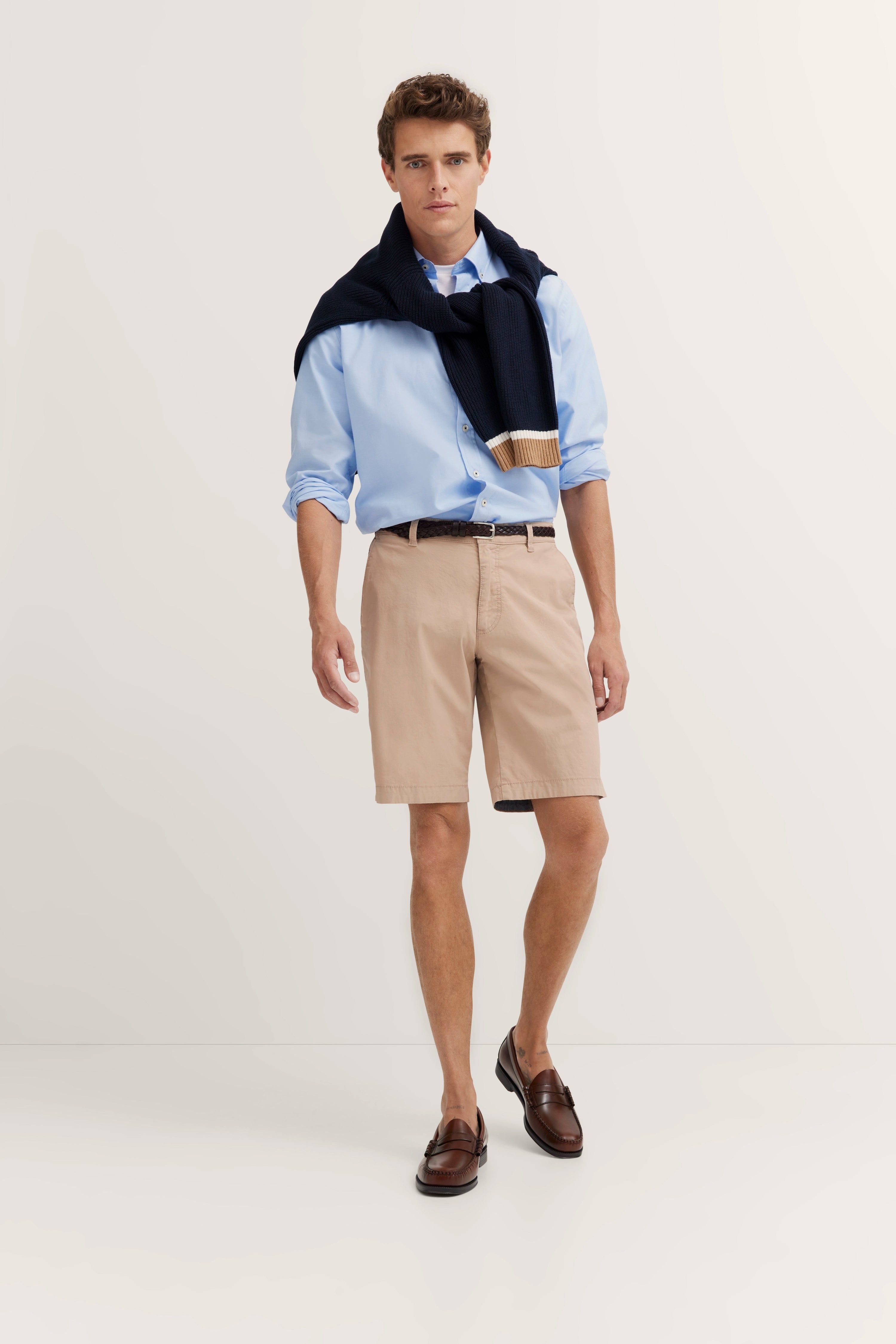 Herren-Shorts in Beige, getragen von Model im legeren Posing, kombiniert mit hellblauem Hemd.