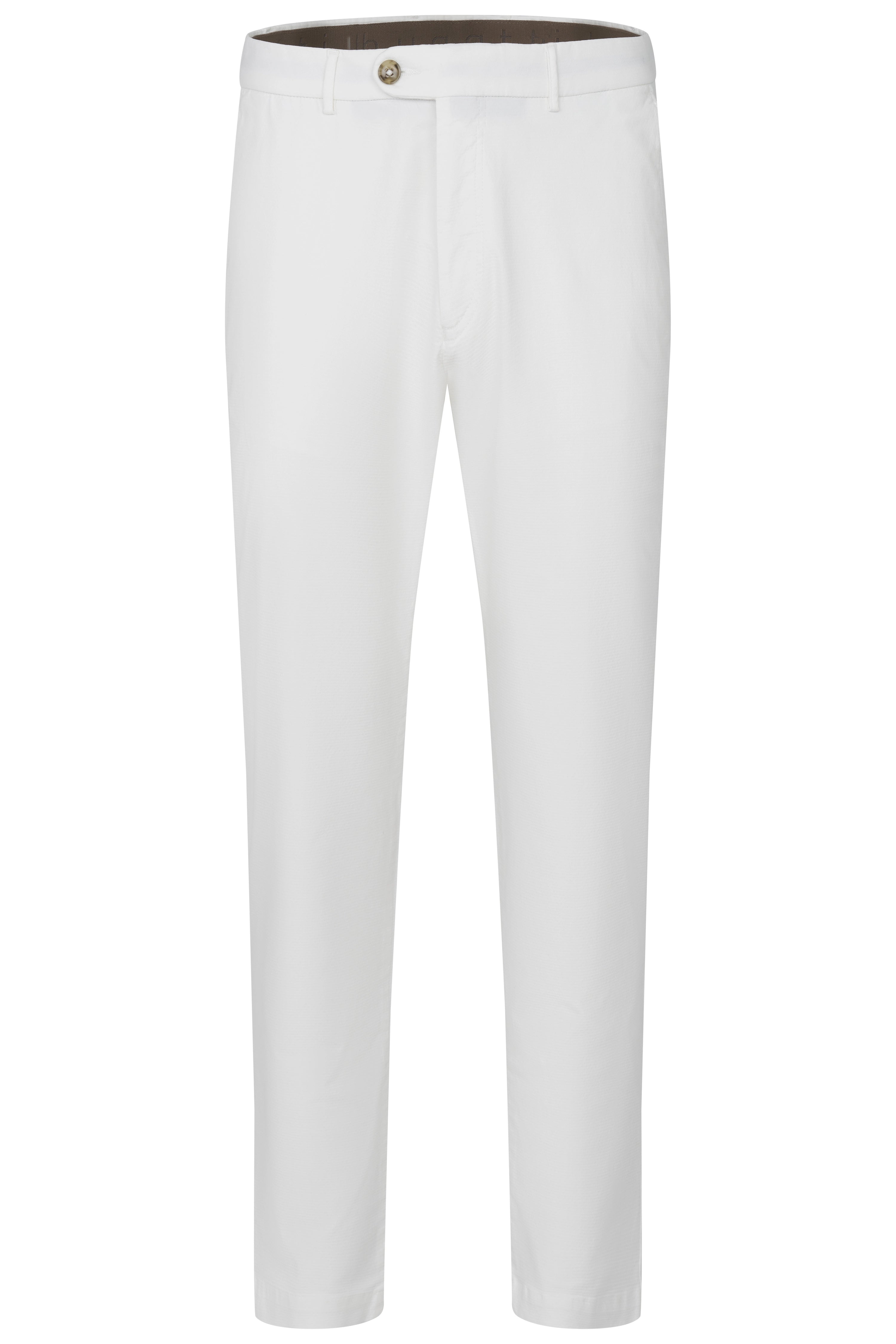 Model in wit overhemd, witte broek, donkerblauwe trui over schouder, bruine sandalen. Ontspannen pose.
