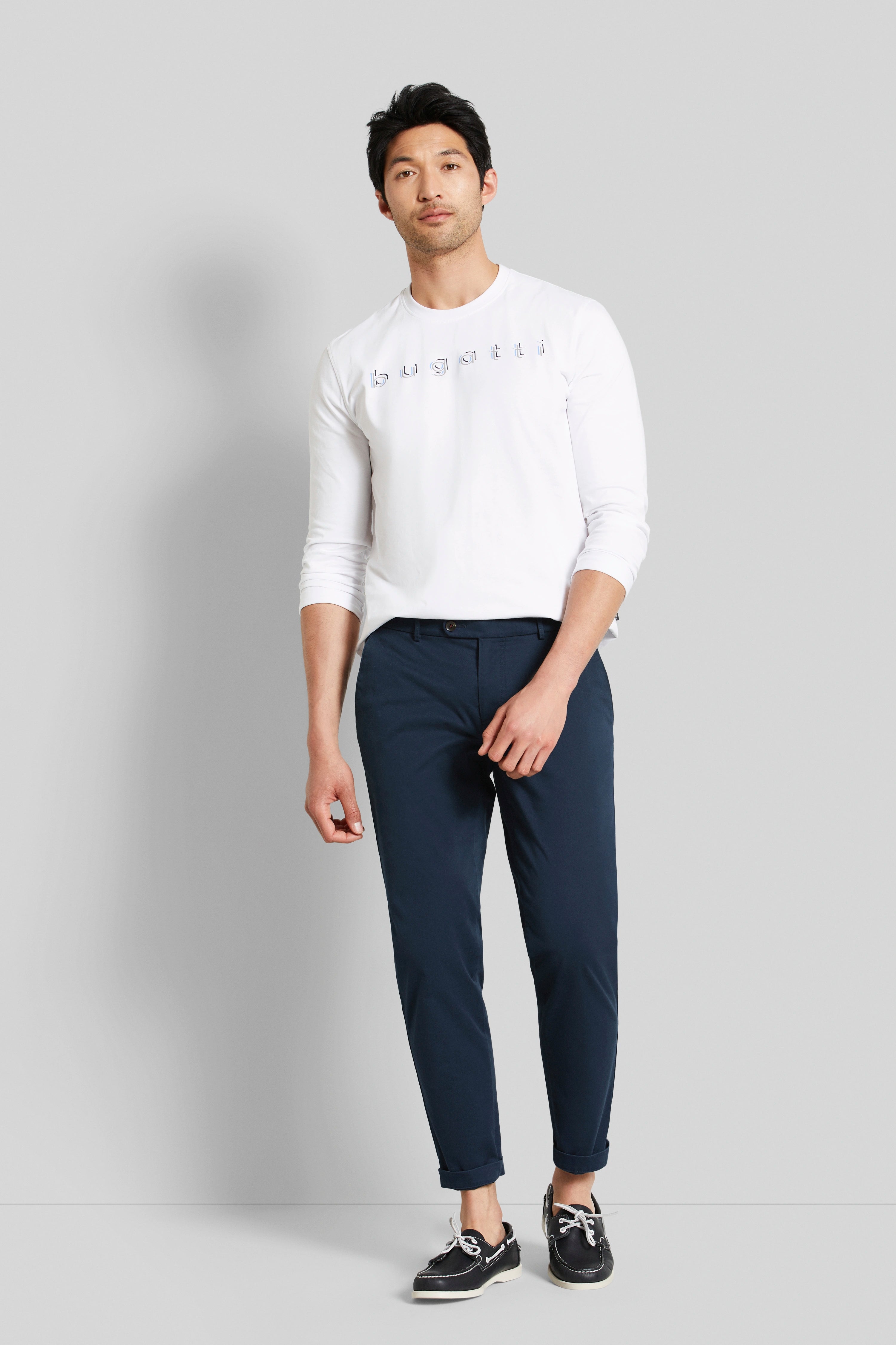 White bugatti logo shirt, blue chinos, model standing relaxed, looking forward, casual outfit.
