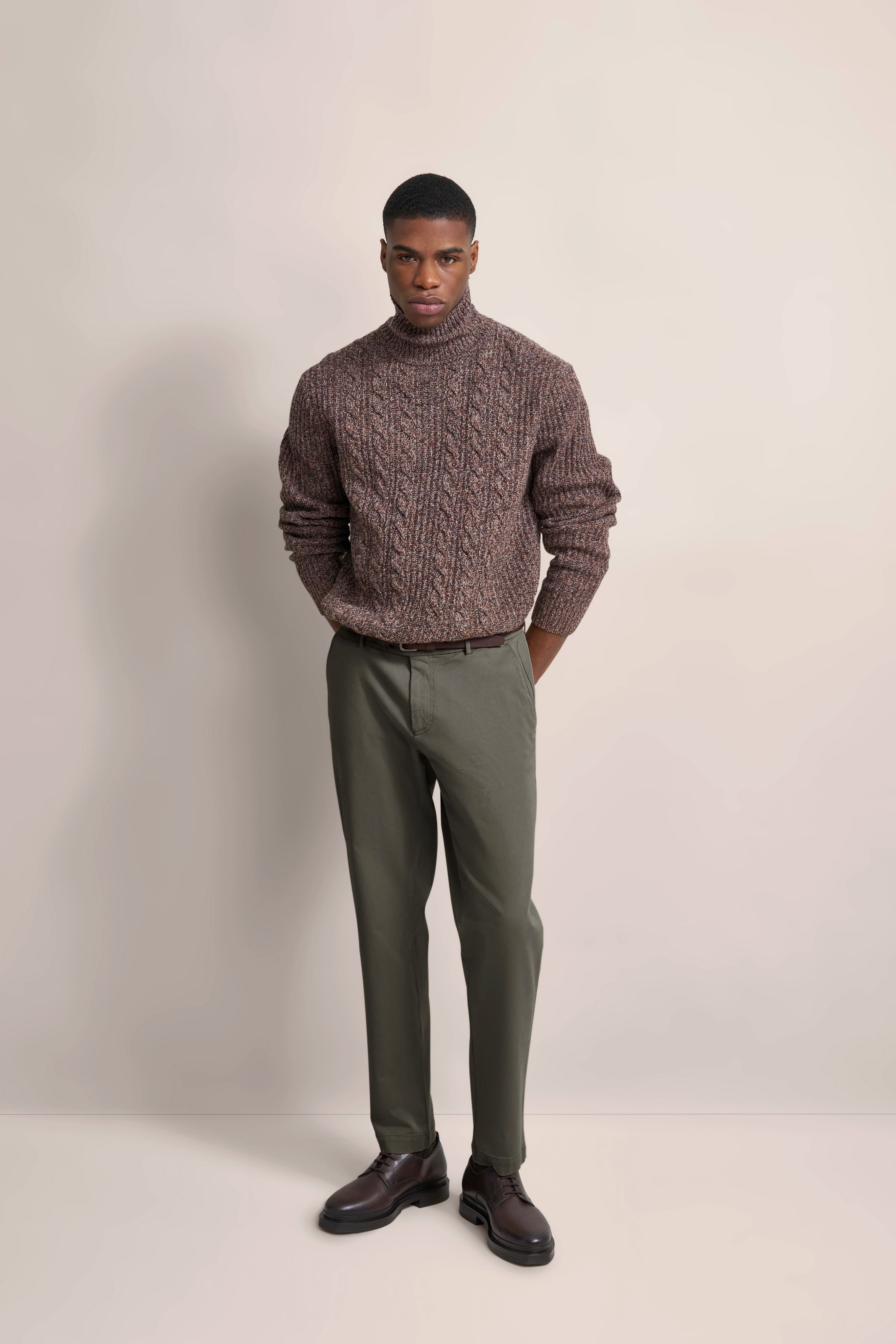 Brown knit sweater, olive green pants, brown shoes, model stands casually with hands in pockets.
