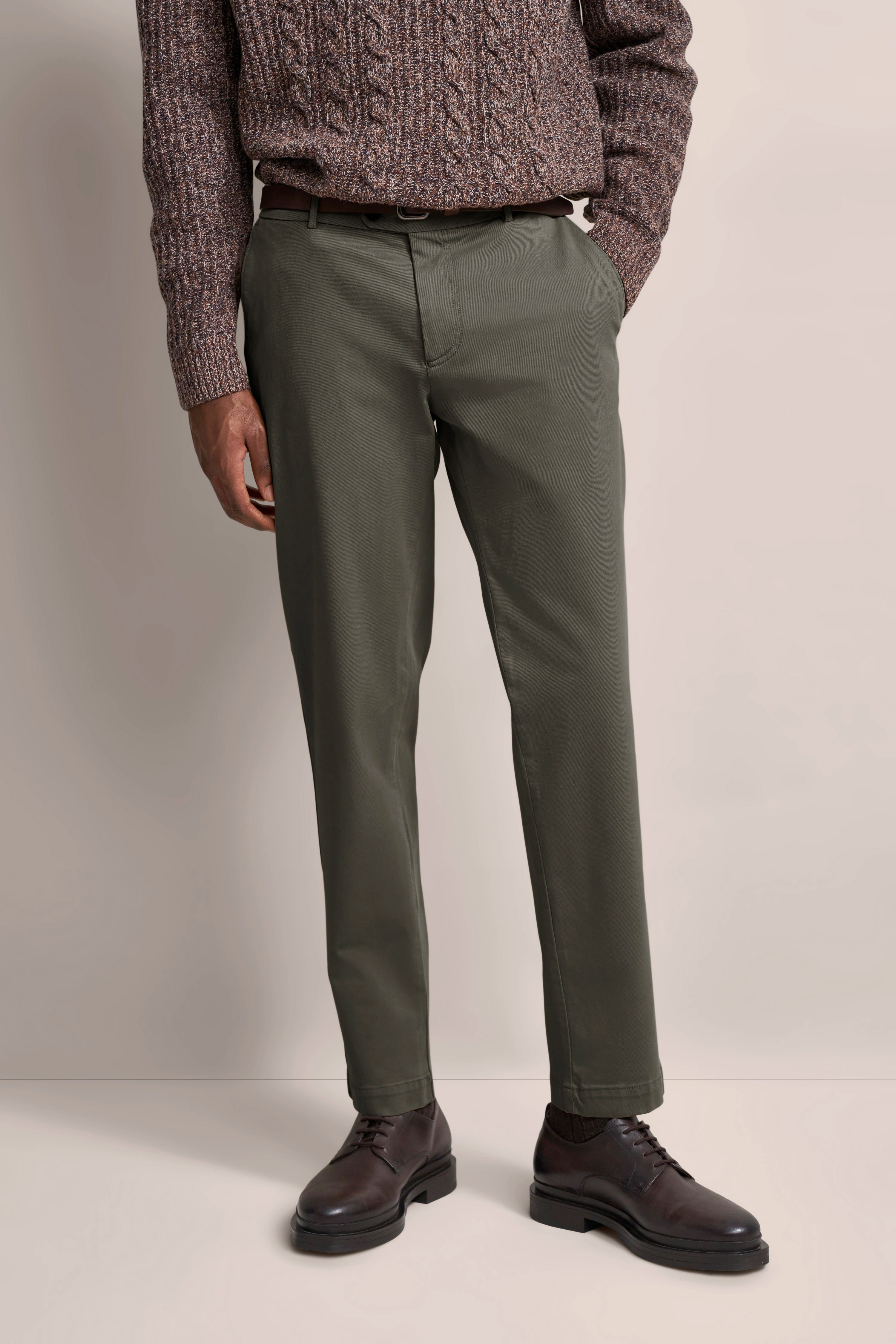 Brown knit sweater with green pants, model posing casually, dark shoes, embodying bugatti's refined lifestyle.