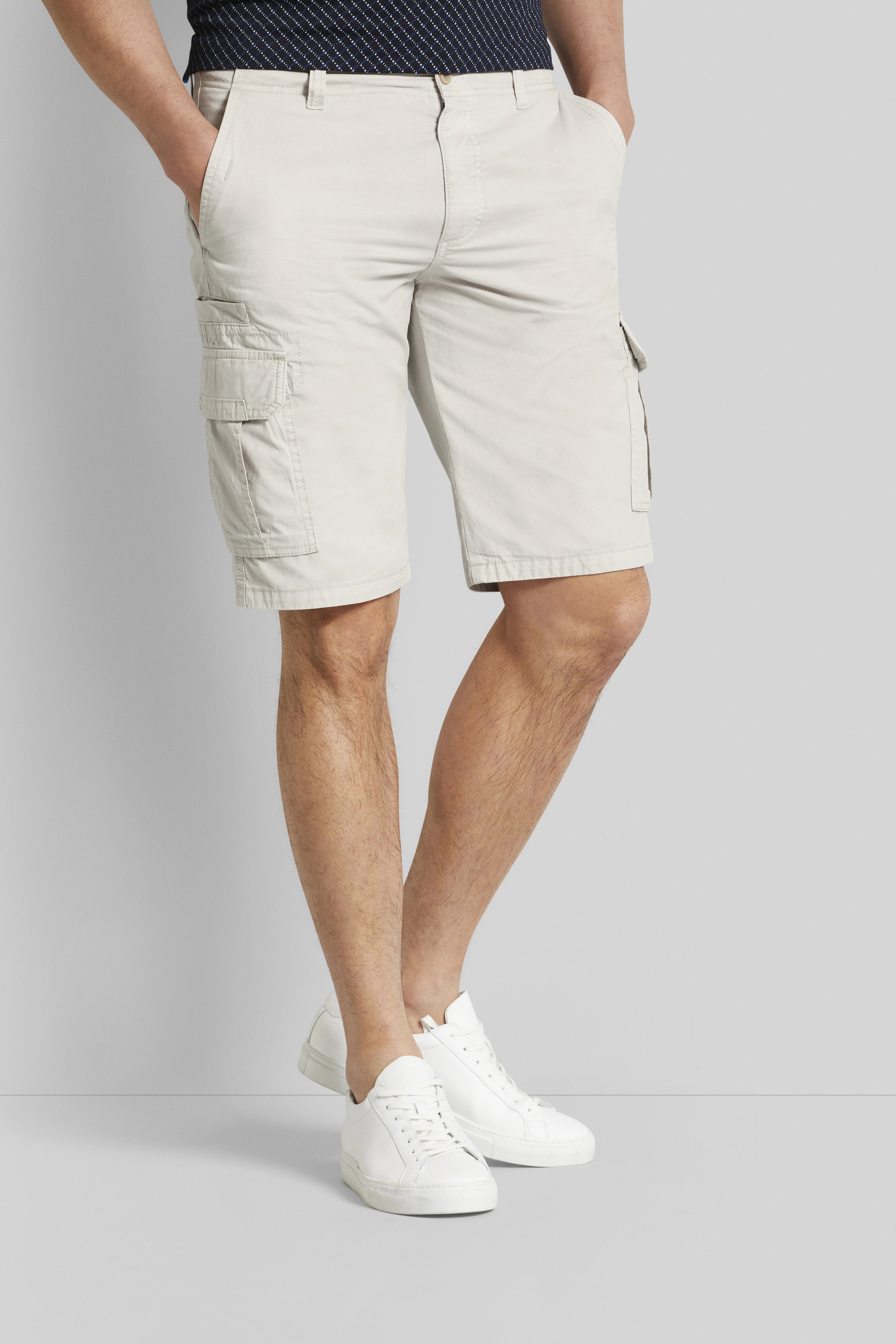 Beige cargo shorts and white shirt, relaxed model, hands in pockets.