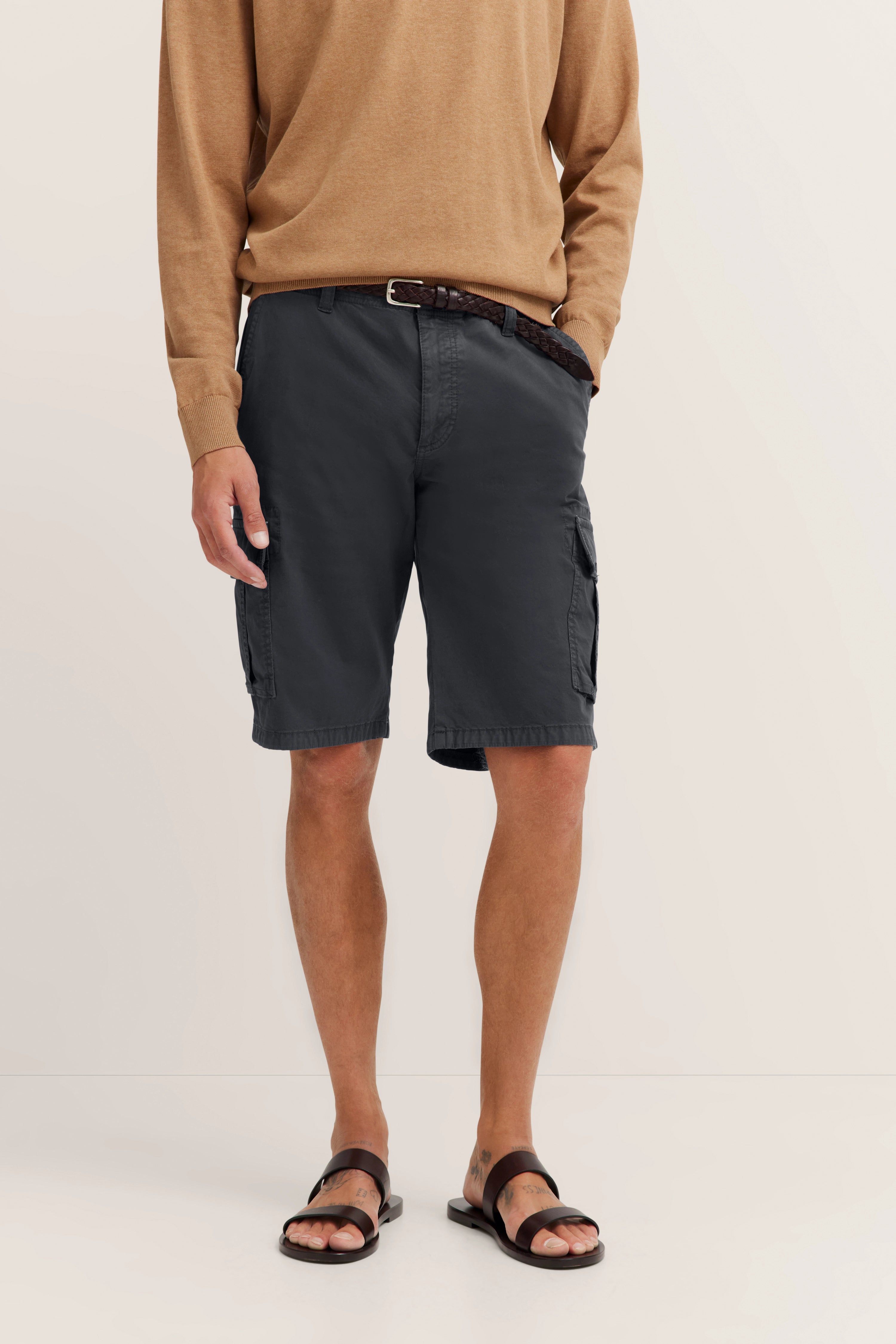 Beiger Pullover, graue Shorts, brauner Gürtel, braune Sandalen, legeres Modelbild, lockere Haltung.