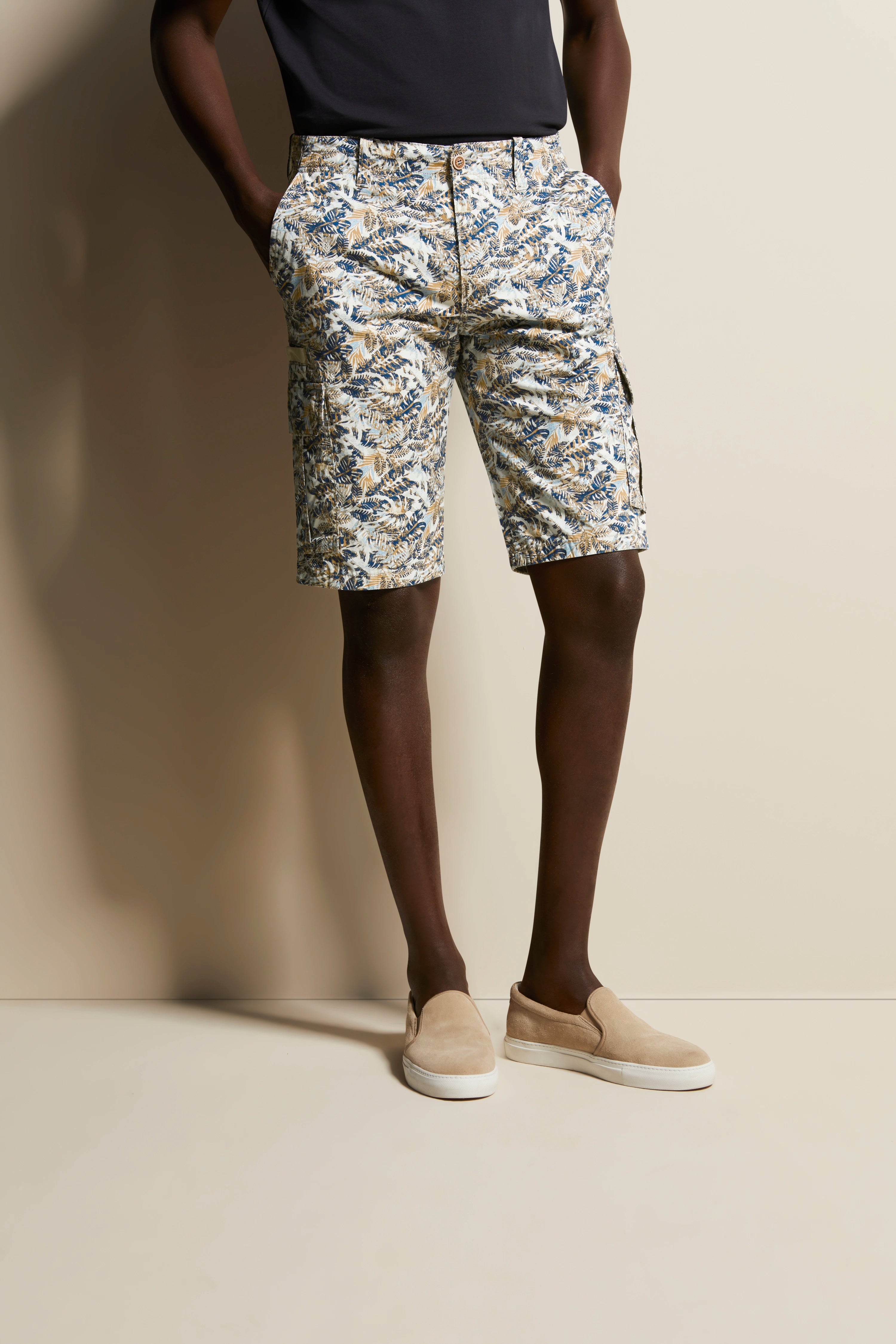 Musterhafte Shorts von bugatti, floral in Blau-Beige, legeres Modelbild, Hände in Taschen, entspannte Pose.