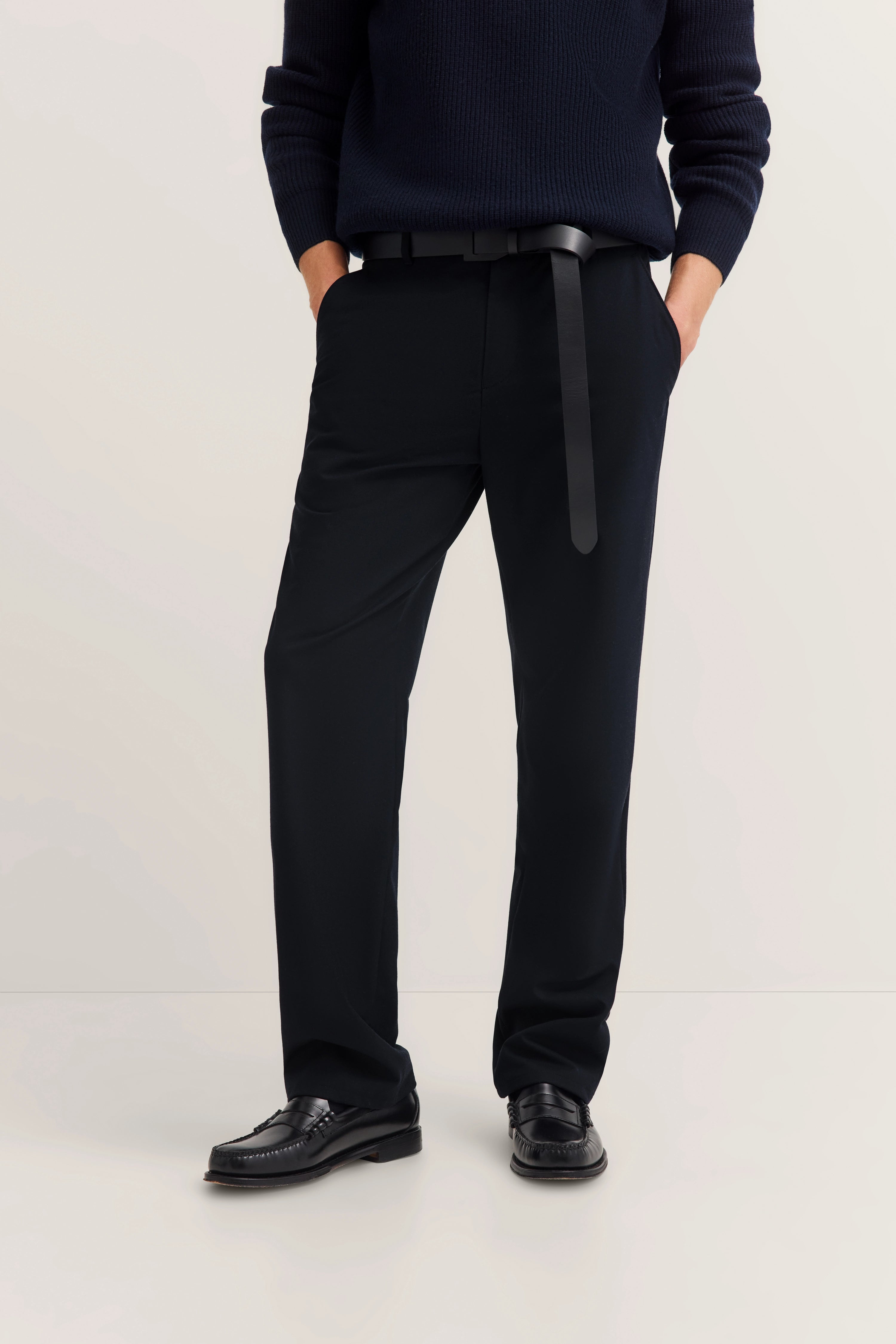 Schwarzer Pullover, schwarze Hose und Schuhe, legeres Modelbild, Hände in den Hosentaschen.