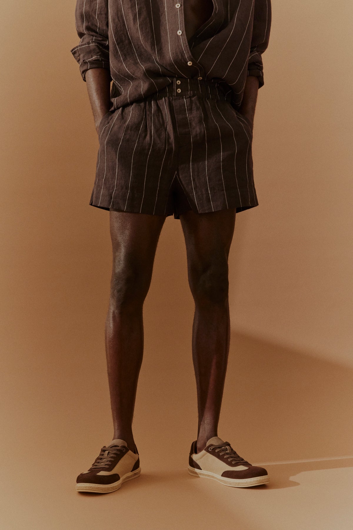 Braunes Nadelstreifen-Shorts-Outfit, legeres Modelbild, Hände in Taschen, Freizeitlook.