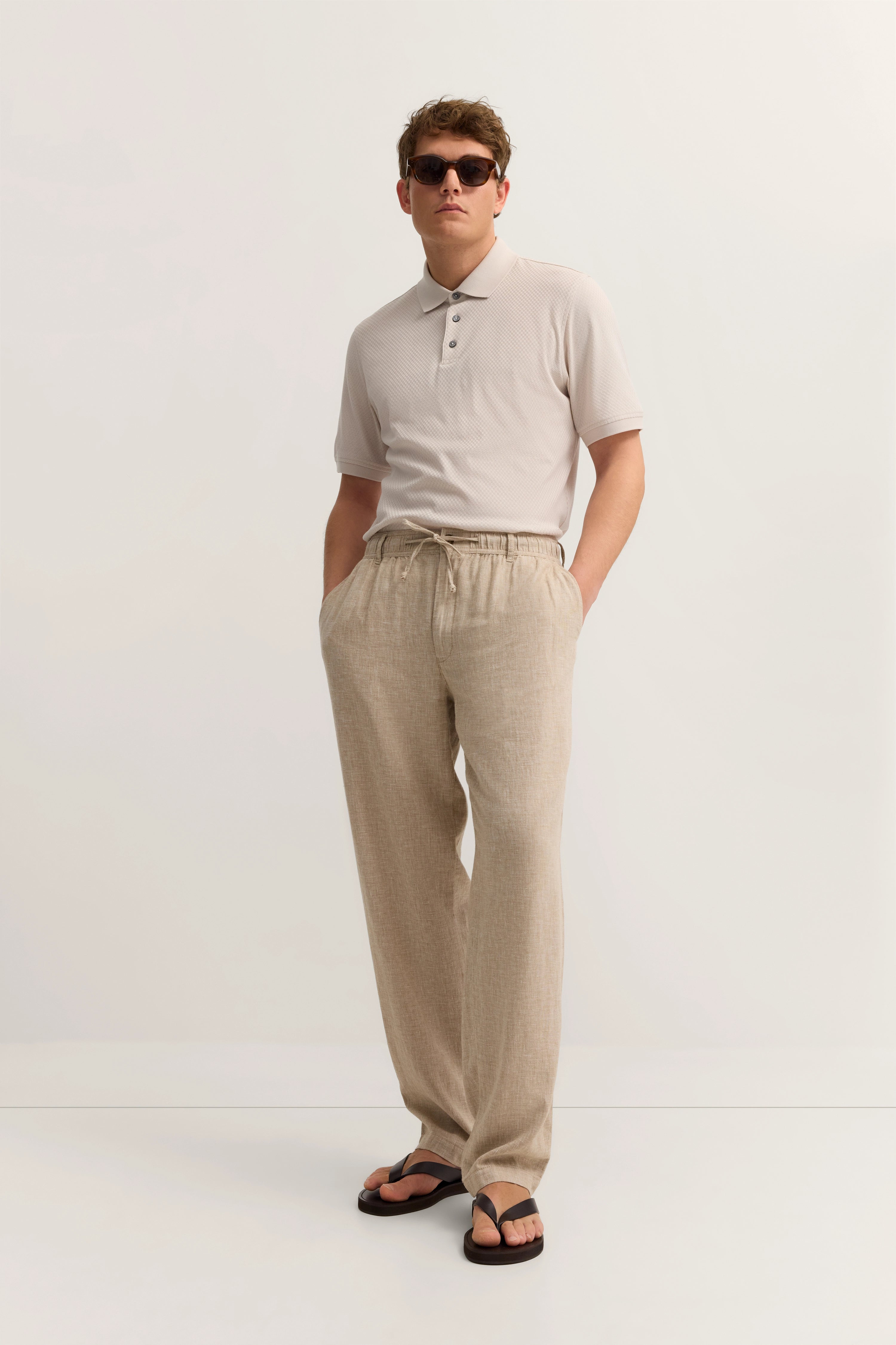 Beiges Polo und Leinenhose, lässiges Model-Pose, Hände in den Taschen, bugatti Stil.