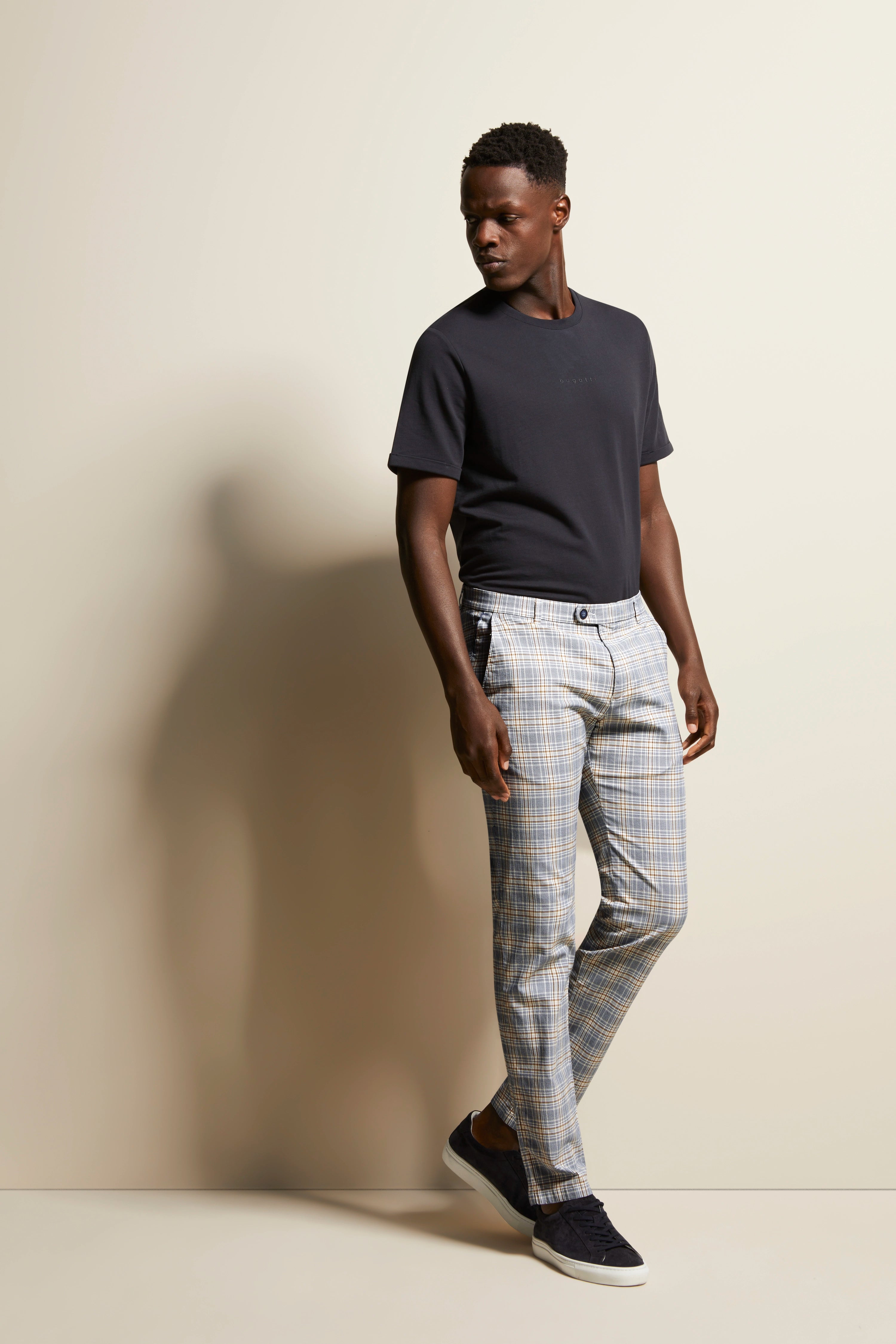Model in zwart bugatti T-shirt, geruite broek, zwarte sneakers, zijwaarts staand.