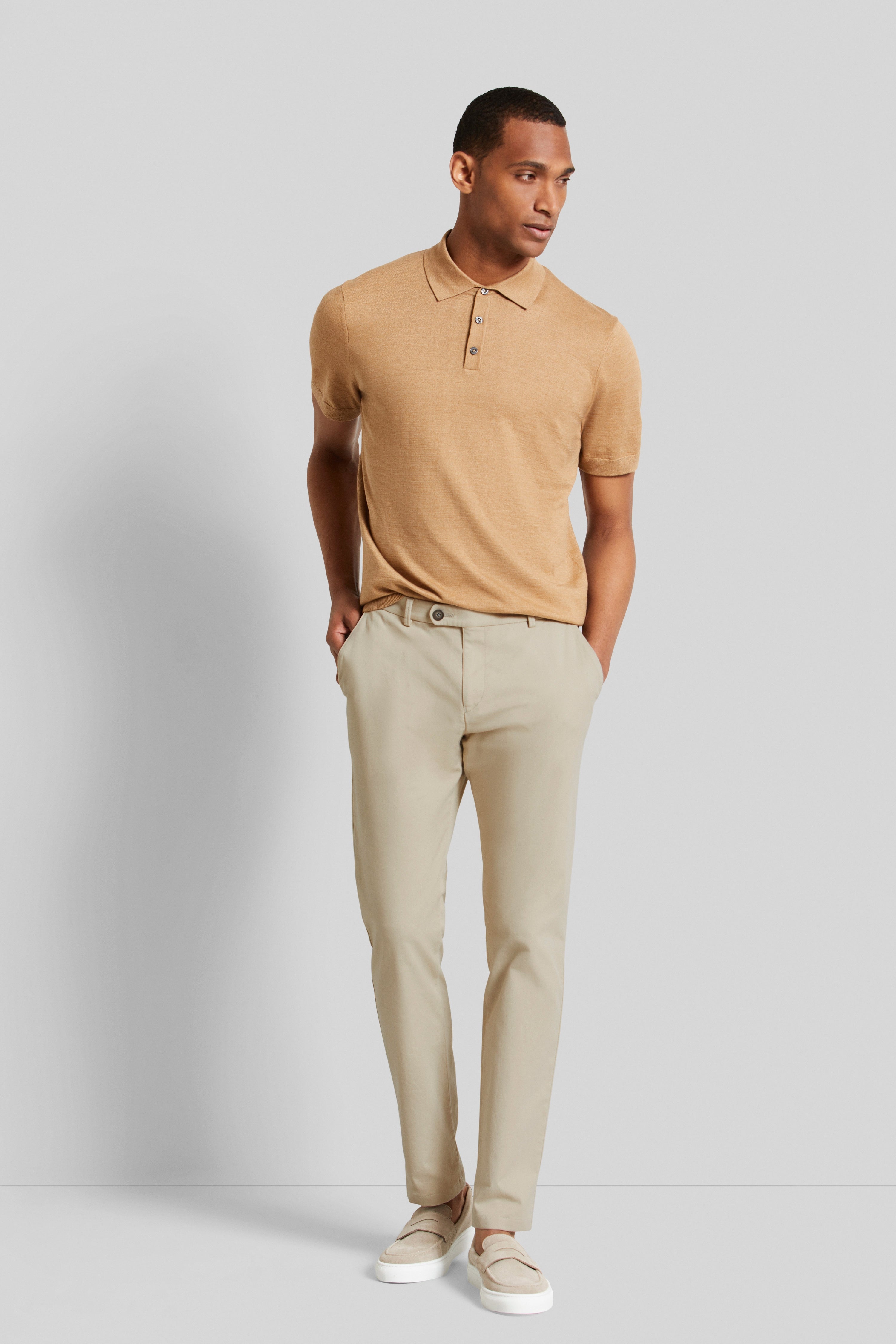 bugatti Modelbild: Beige Chinohose, legerer Look, Rückenansicht, kombiniert mit braunem Oberteil und hellen Schuhen.