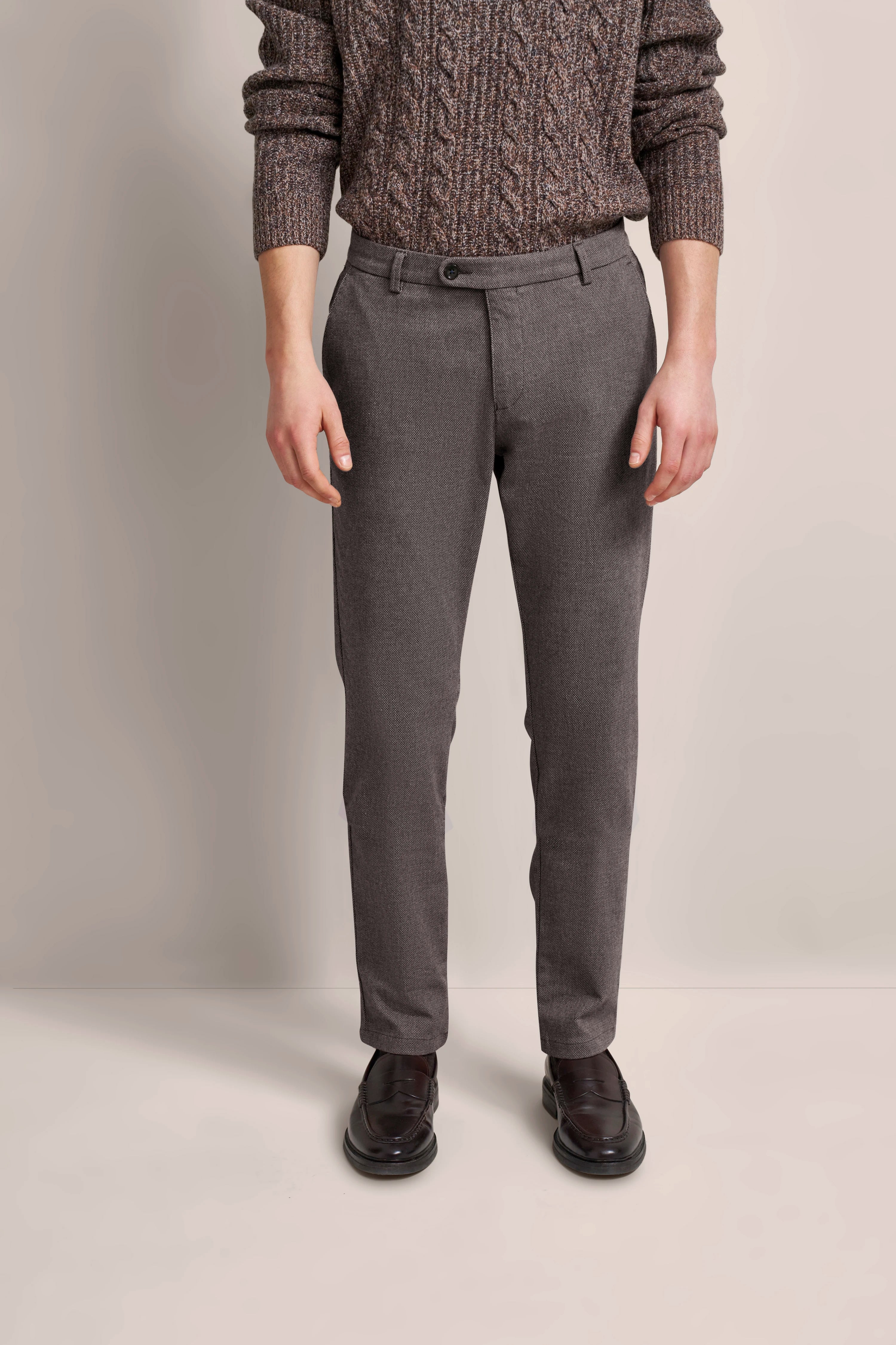 Elegantes bugatti-Modelbild: brauner Strickpullover, graue Hose, schwarze Schuhe, leger stehend.