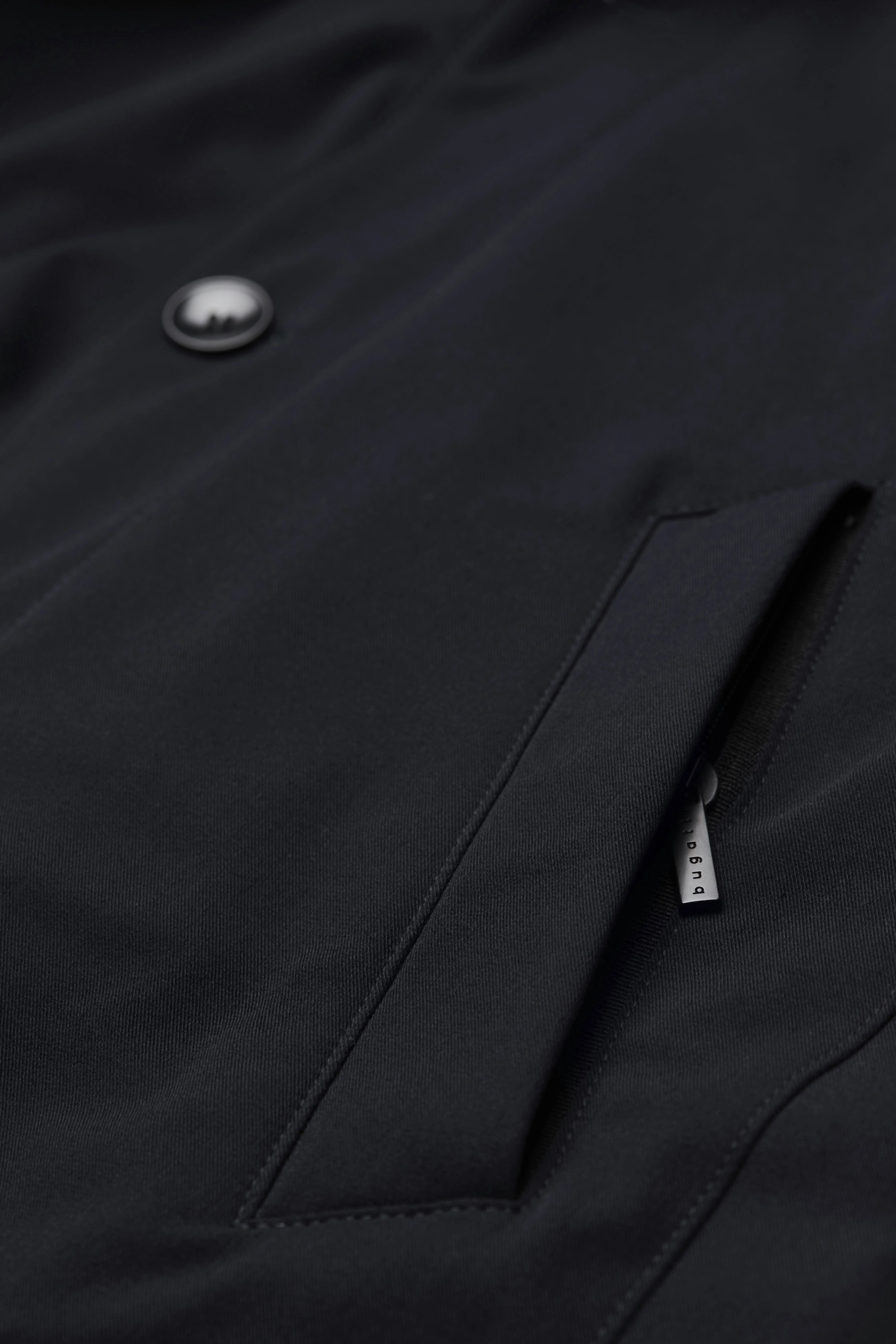 Schwarze bugatti Jacke, Detailaufnahme mit Knopf und Reißverschluss, hochwertiges Material.