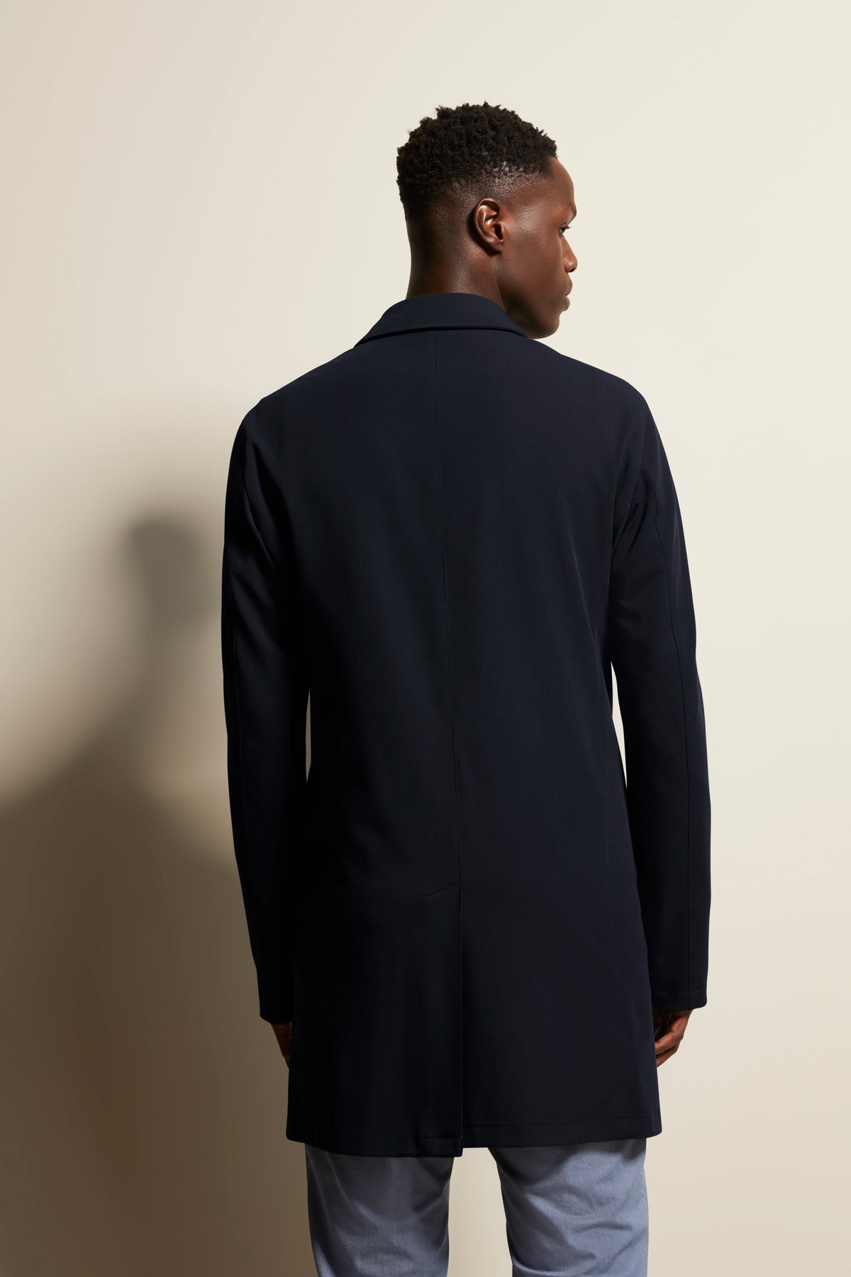 Back view of model in black bugatti coat and gray pants, relaxed pose.