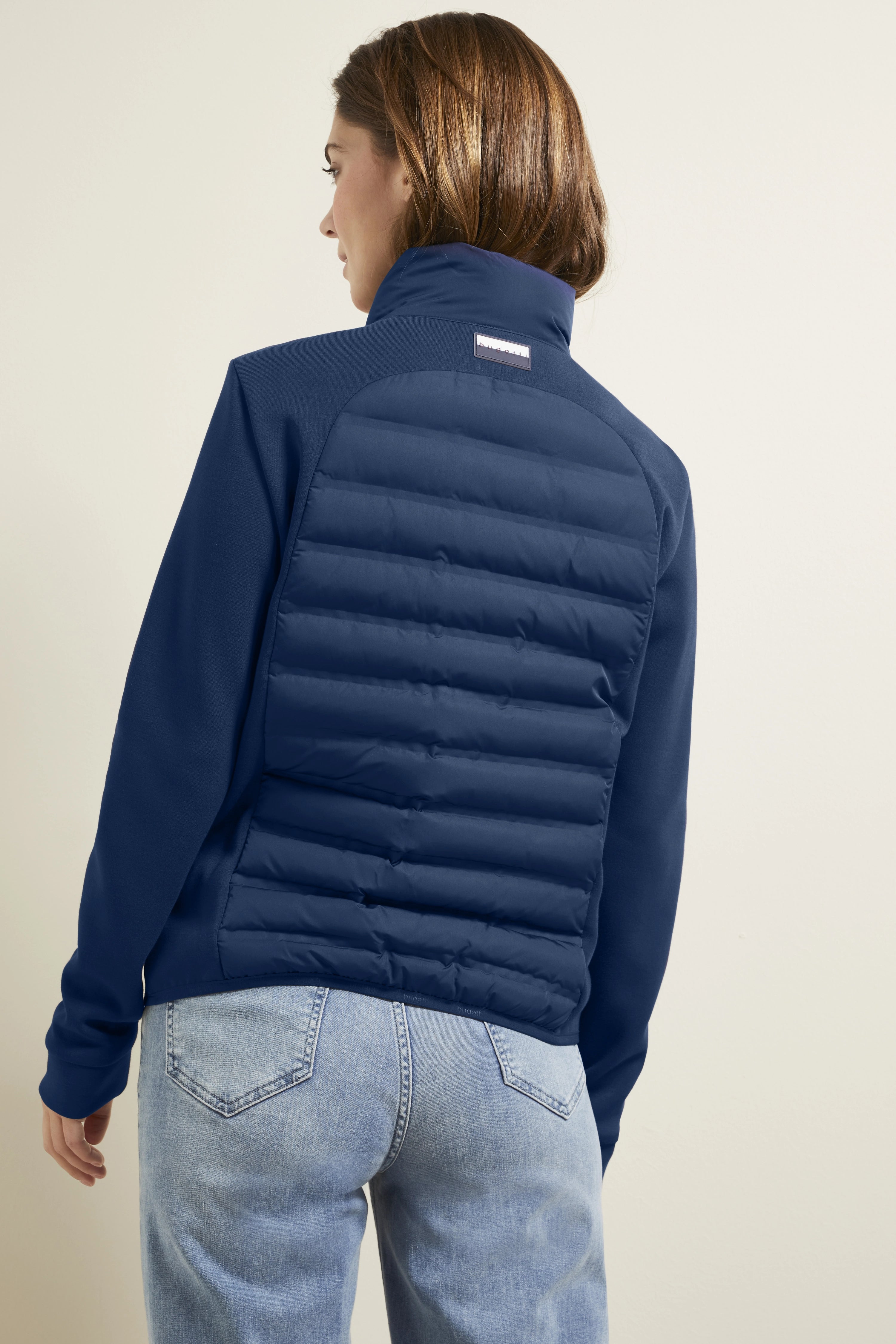 Model in blauwe bugatti jas, rugaanzicht, ontspannen pose, lichte jeans.