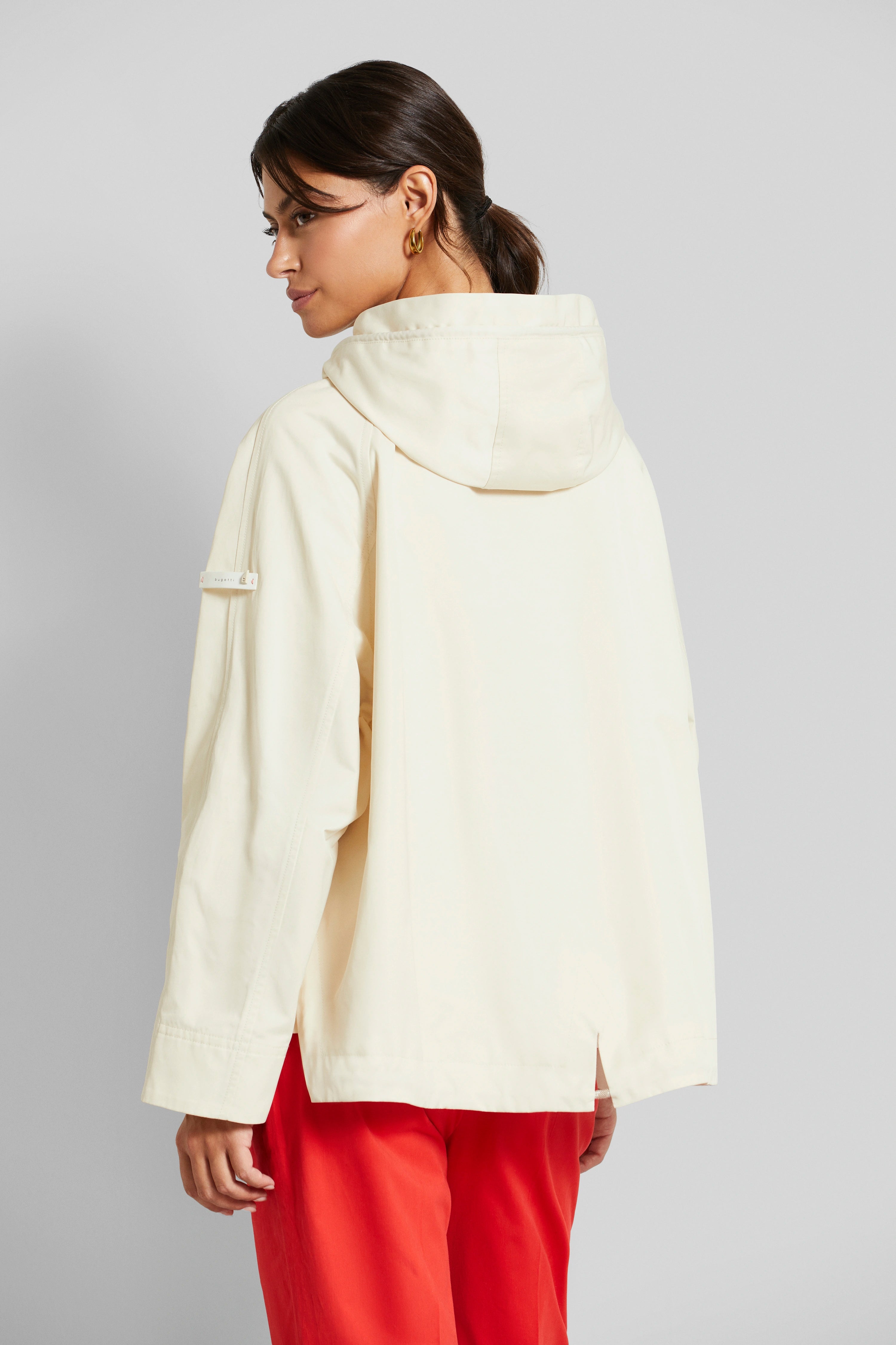 Modelbild mit Rückansicht: Cremefarbene Jacke von bugatti, rote Hose, gelassenes Posing.