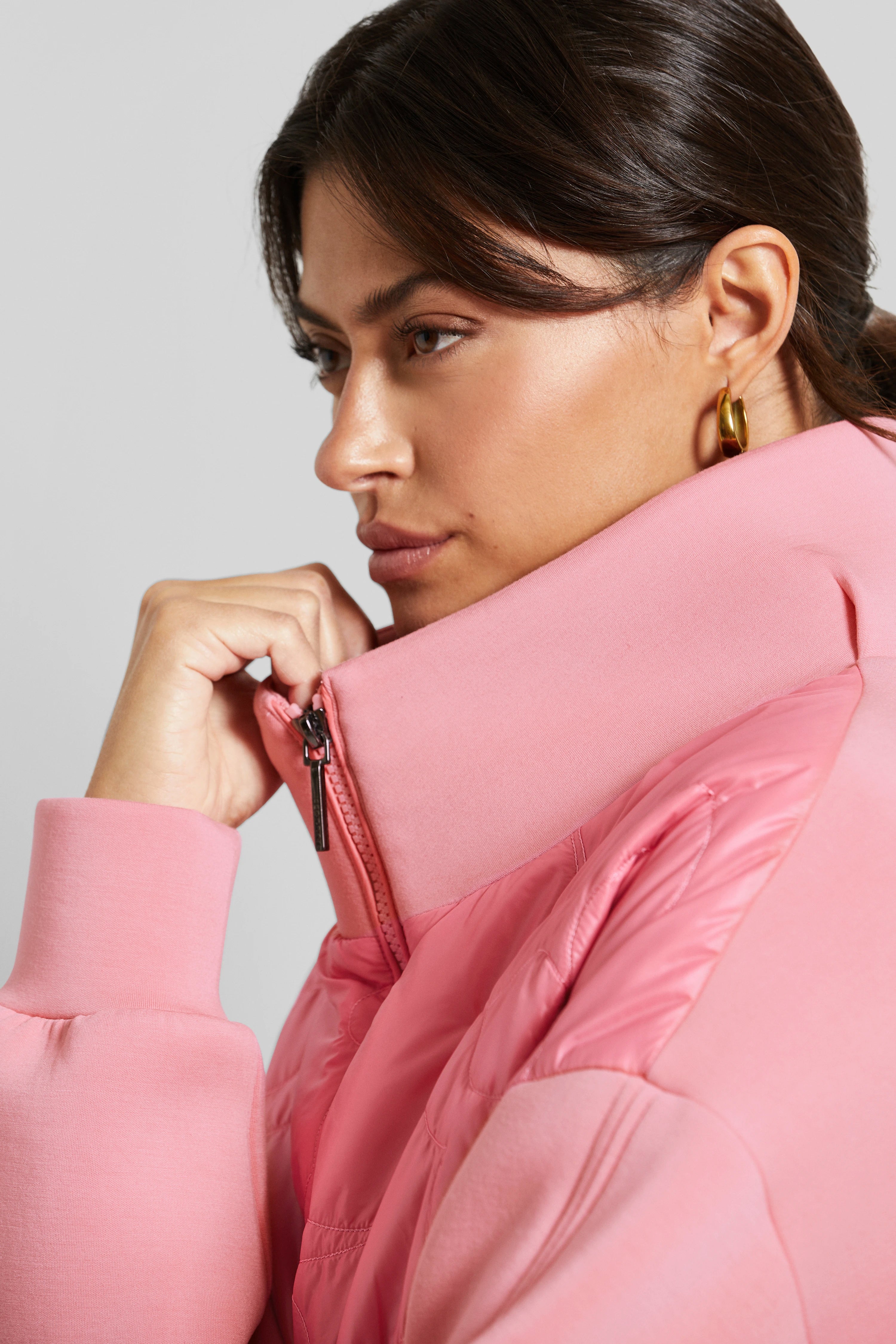 Model wearing pink bugatti quilted jacket, gold earrings, side pose.