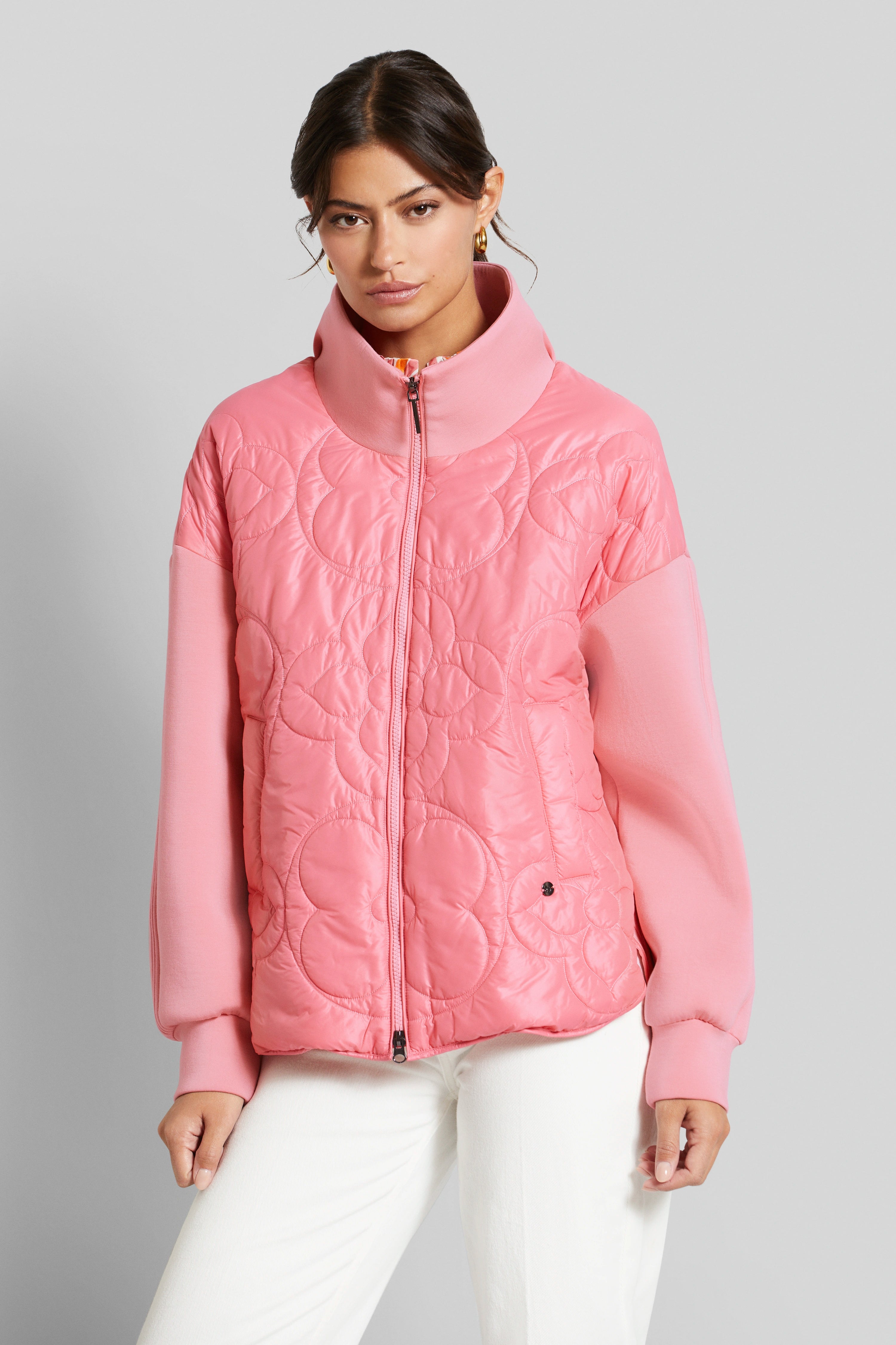 Model wears pink bugatti quilted jacket, casual pose, paired with white trousers.