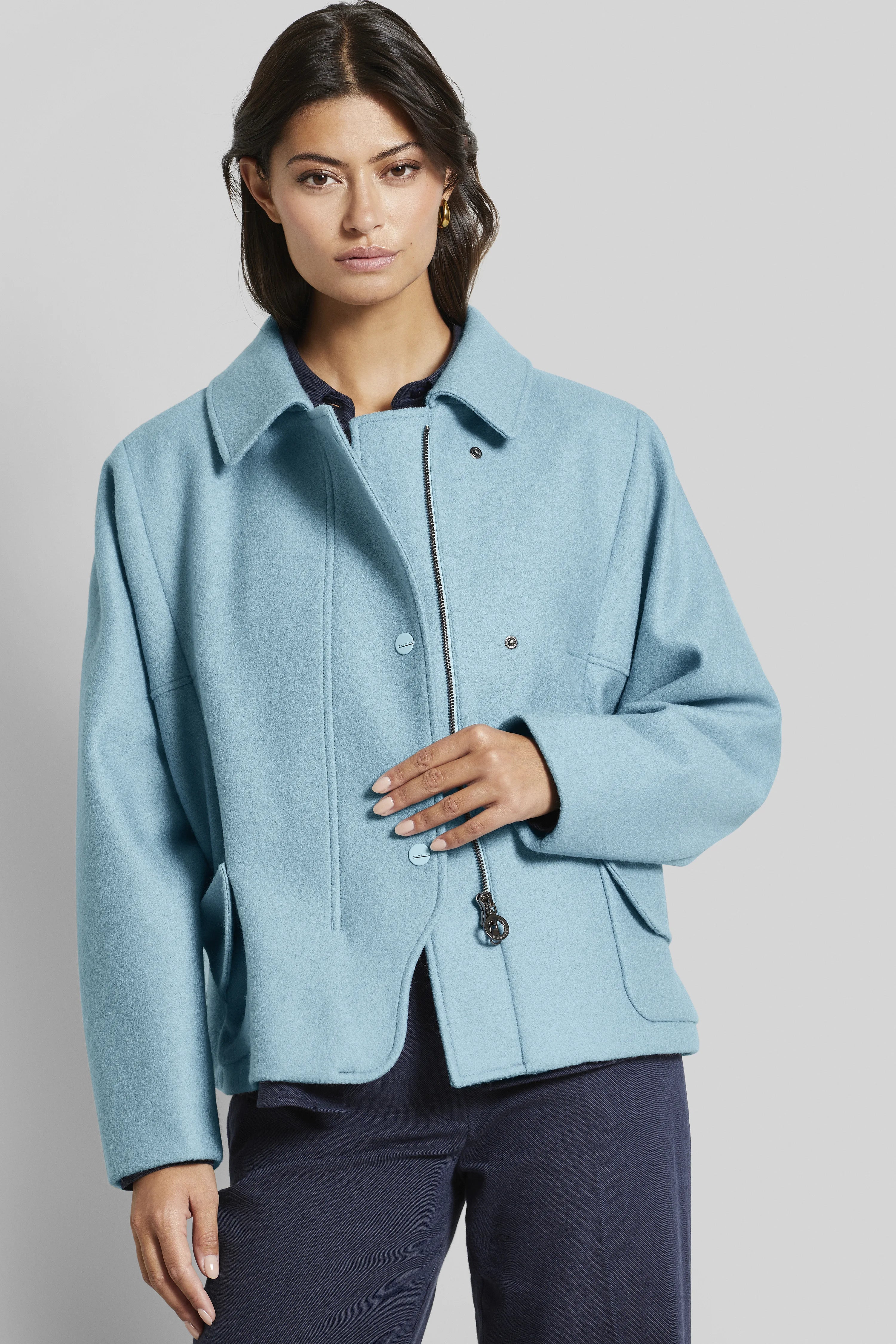 Model in lichtblauw bugatti jack, ontspannen pose, met donkerblauwe broek.
