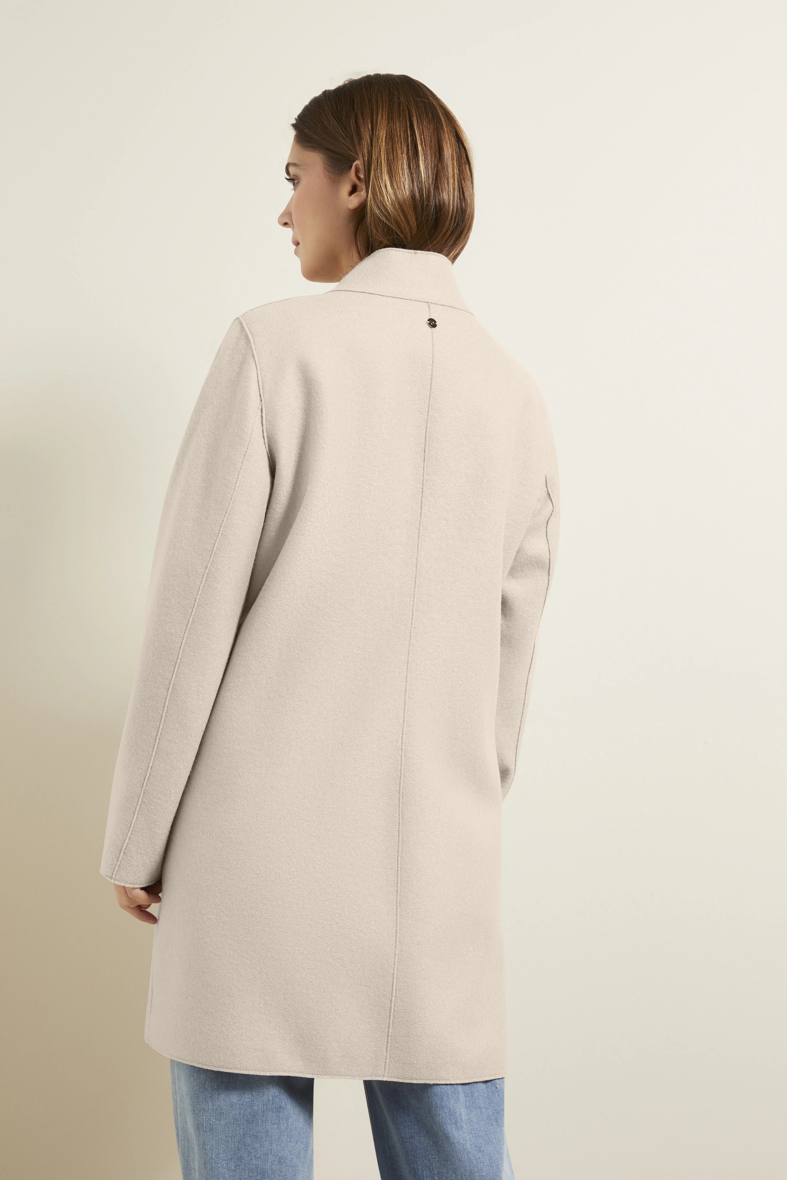 Beigefarbener bugatti Mantel auf Model, Seitenansicht, kombiniert mit blauen Jeans.