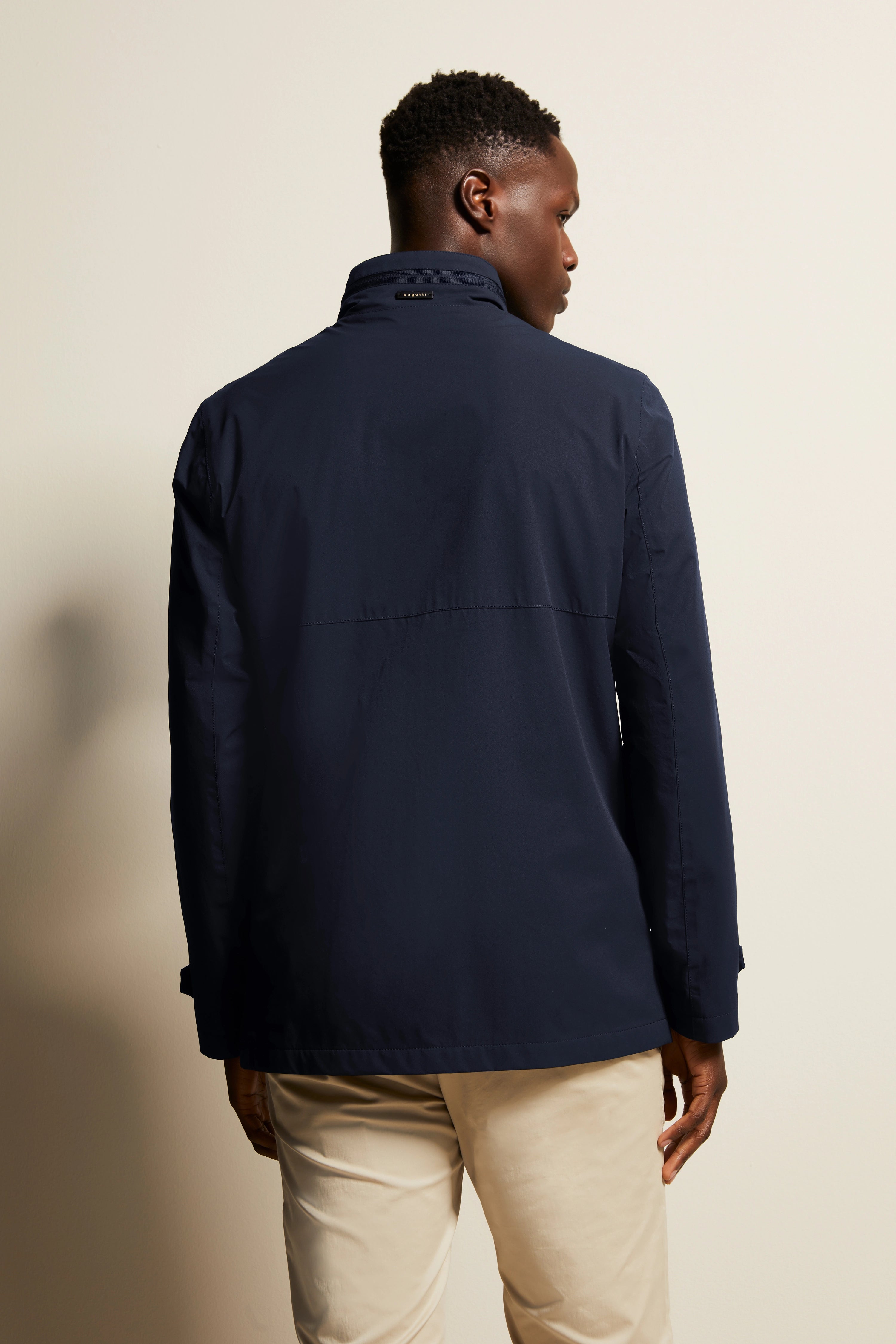 Dunkelblaue bugatti Jacke, Modelbild von hinten, lässige Pose, beige Hose.