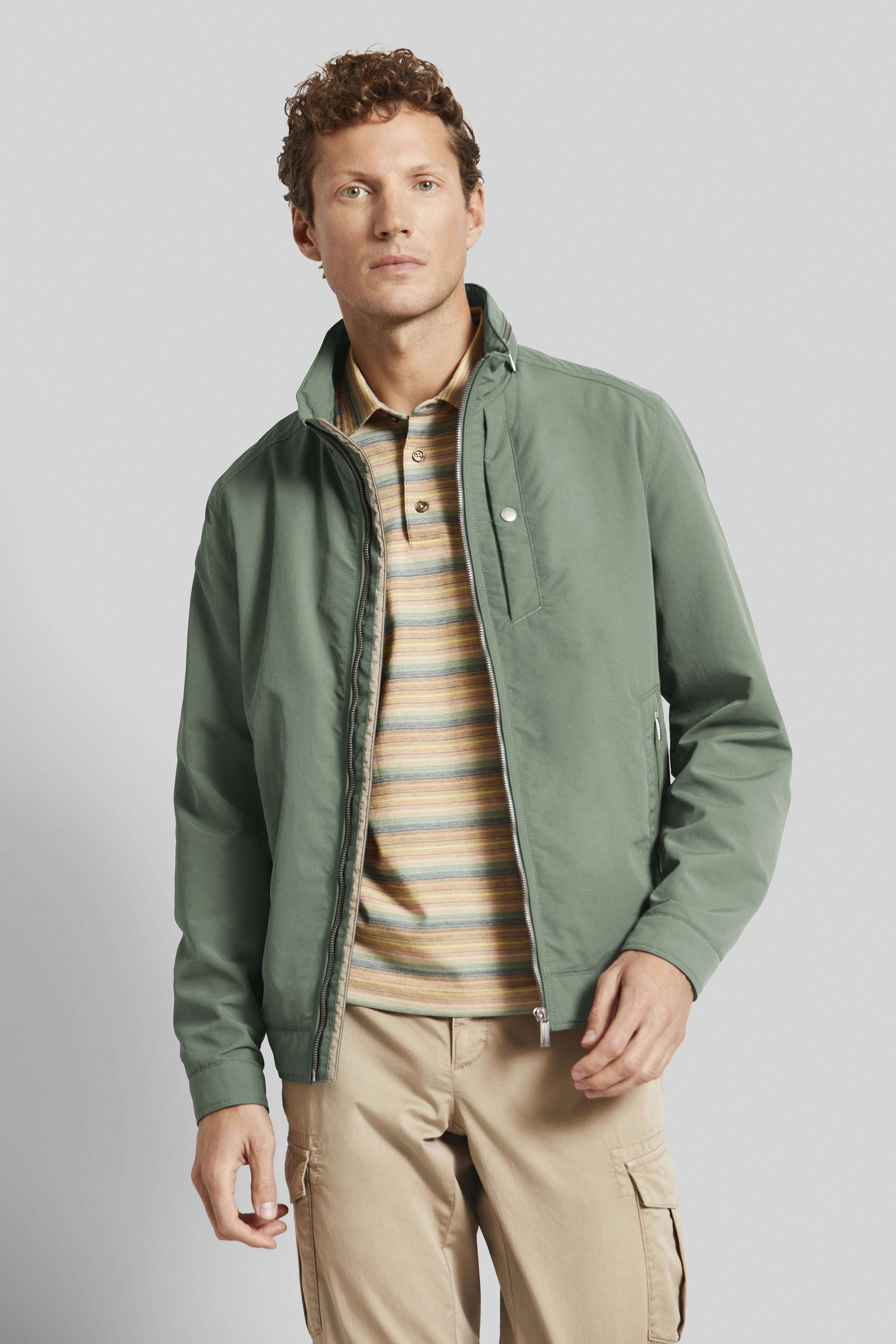 Green bugatti jacket, striped polo, beige cargo pants, model stands casually.