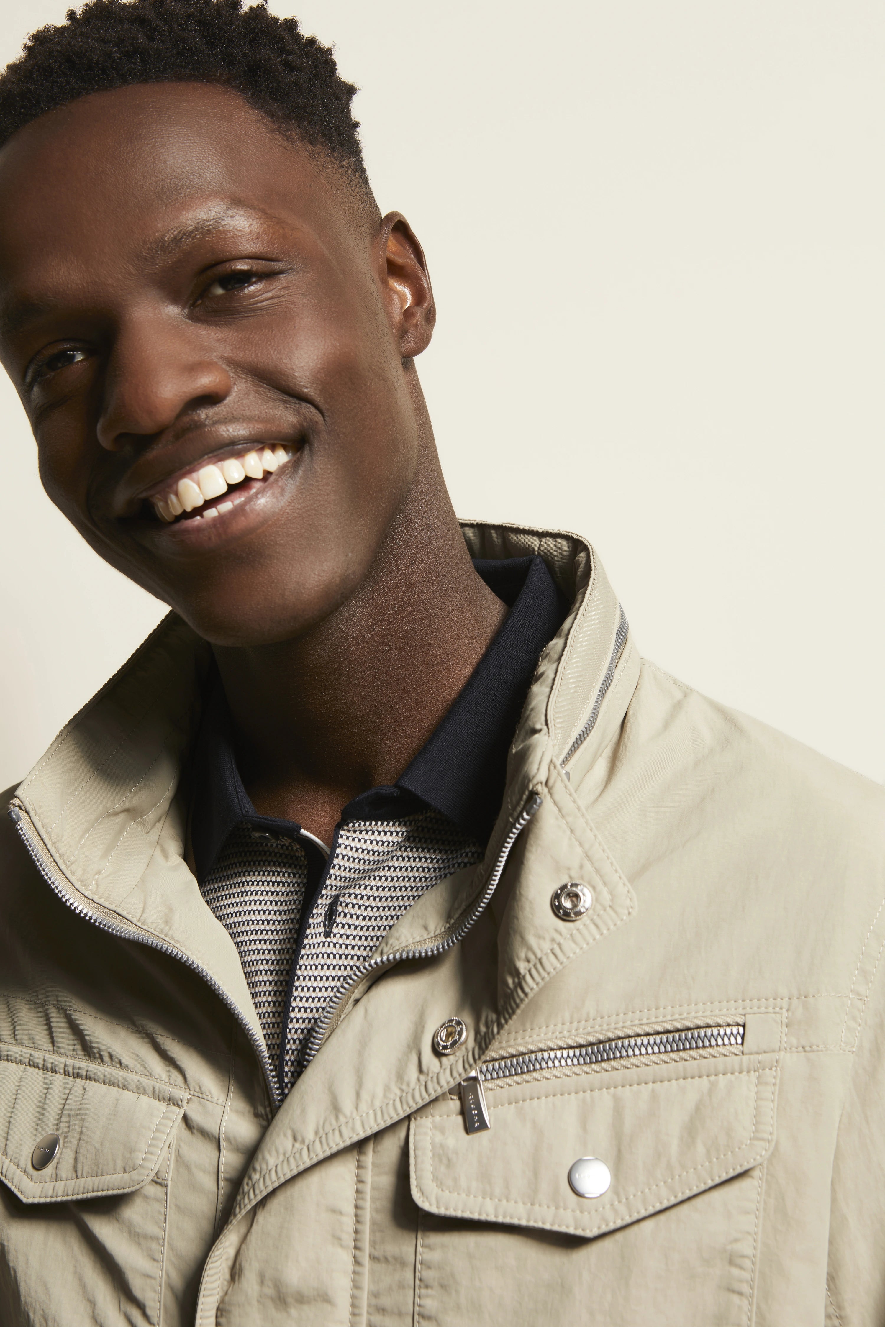 Beiges bugatti-Outfit mit Steppjacke und gemustertem Poloshirt, Model lächelt, Nahaufnahme.