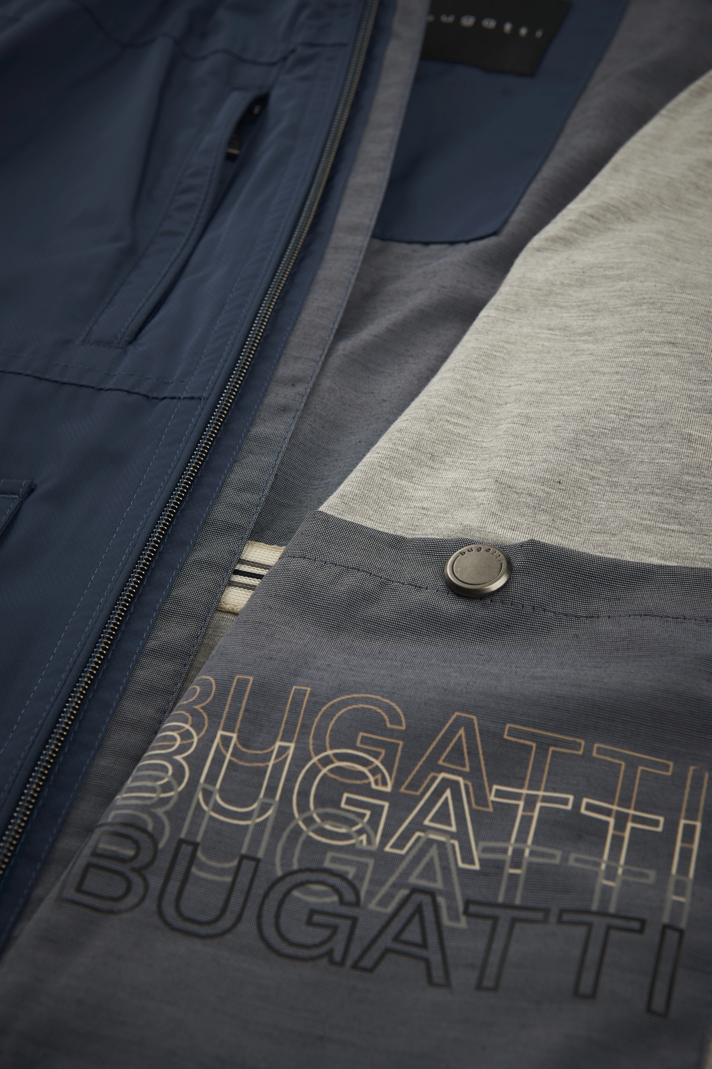 Navy Jacke und graues Shirt mit bugatti-Logo, Detailaufnahme.