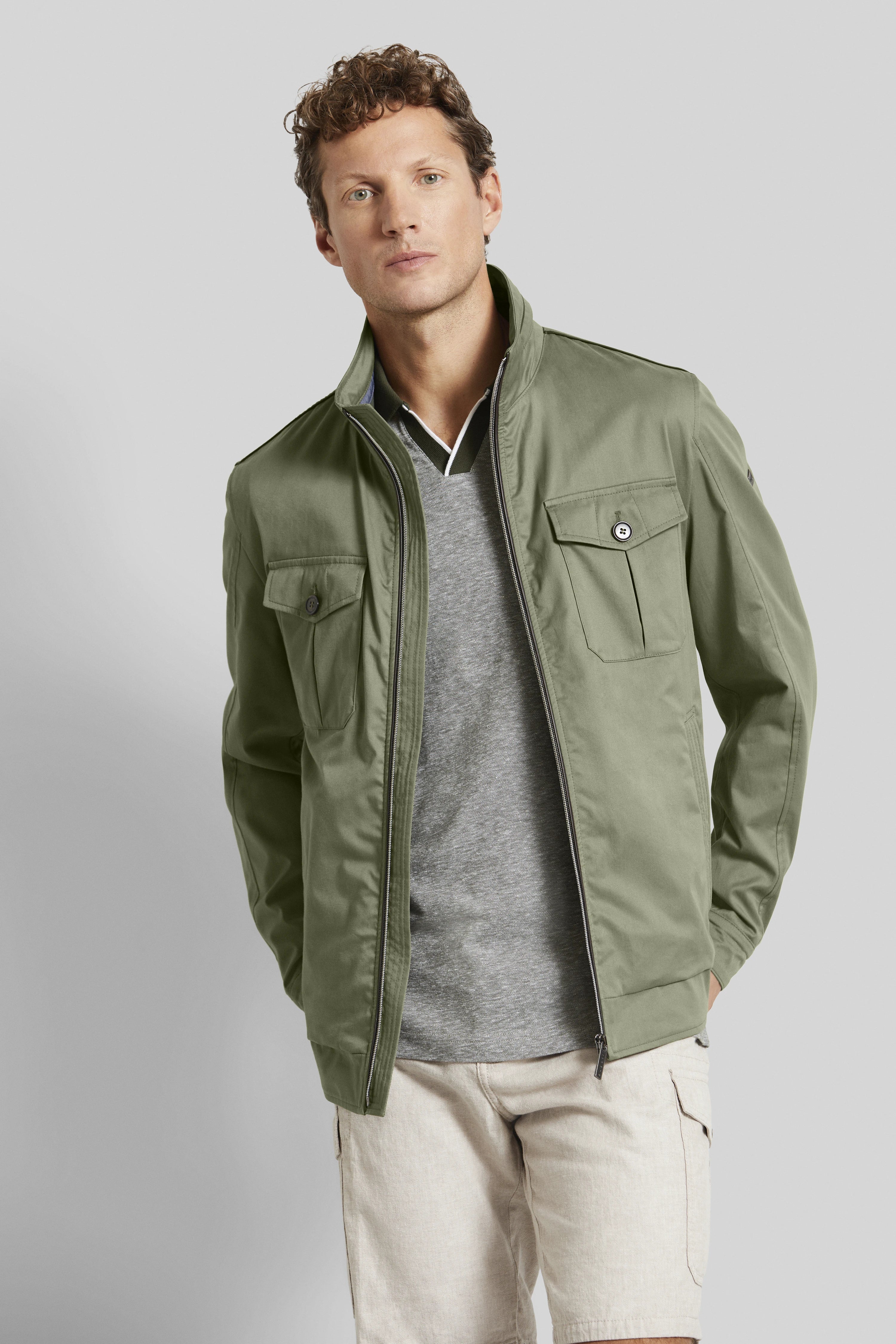 Model in olivgrüner bugatti Jacke, grauem Shirt und beigen Shorts, legeres Posing.