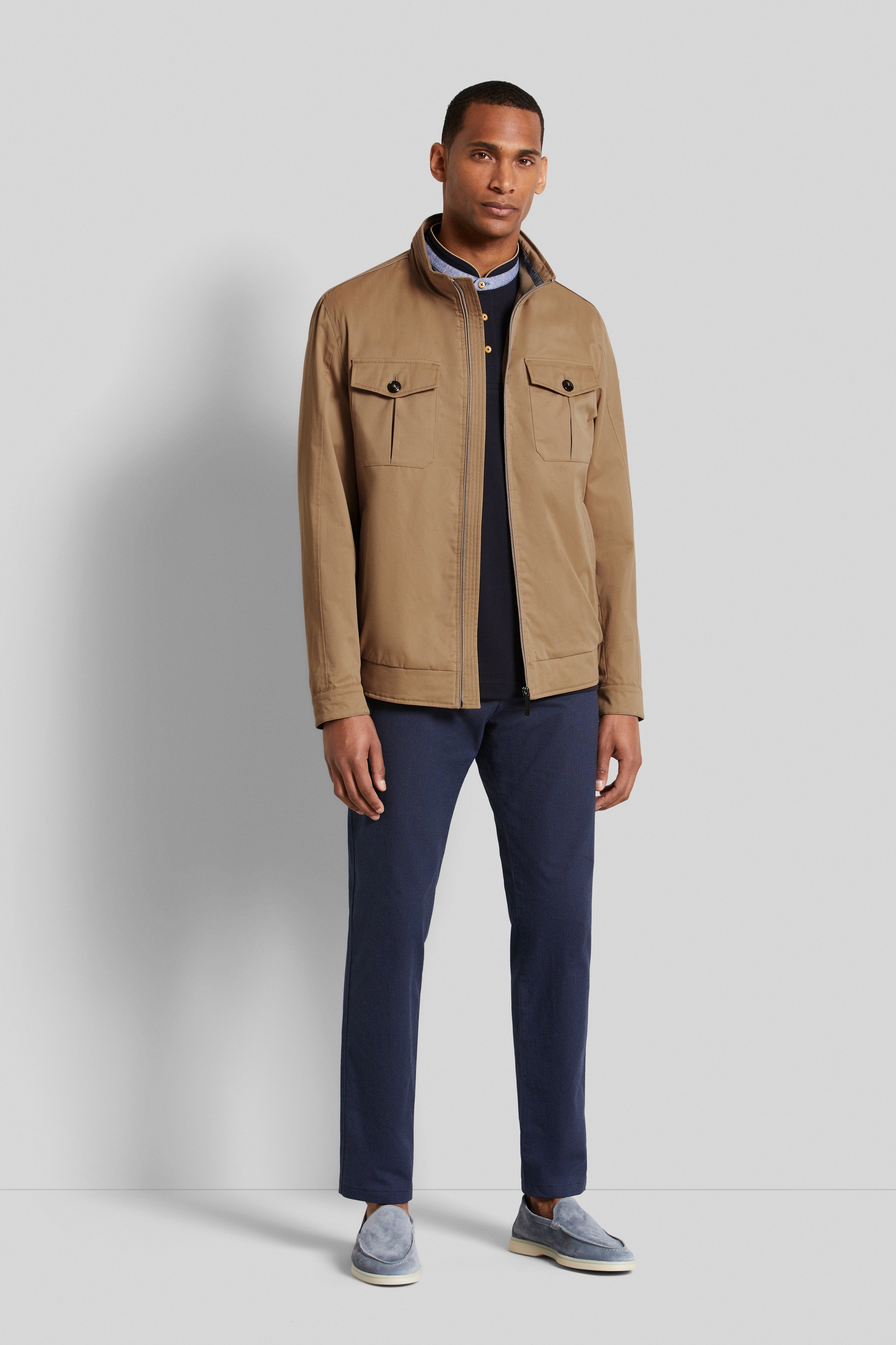 Model trägt khakifarbene Jacke, dunkelblauen Pullover, blaue Hose, blaue Slipper