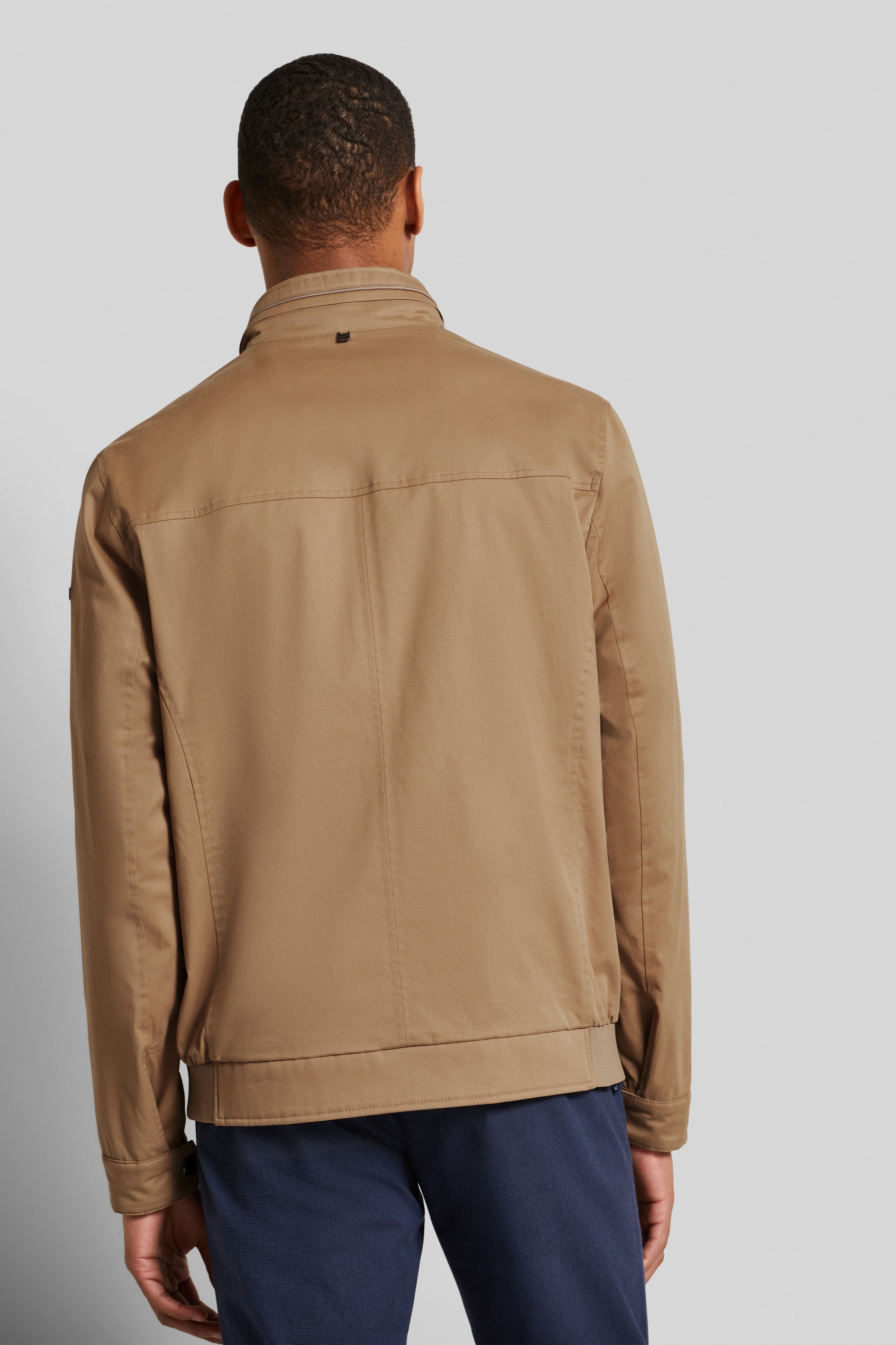 bugatti Modelbild, beige Jacke, Rückenansicht, lässiger Stand, blaue Hose.