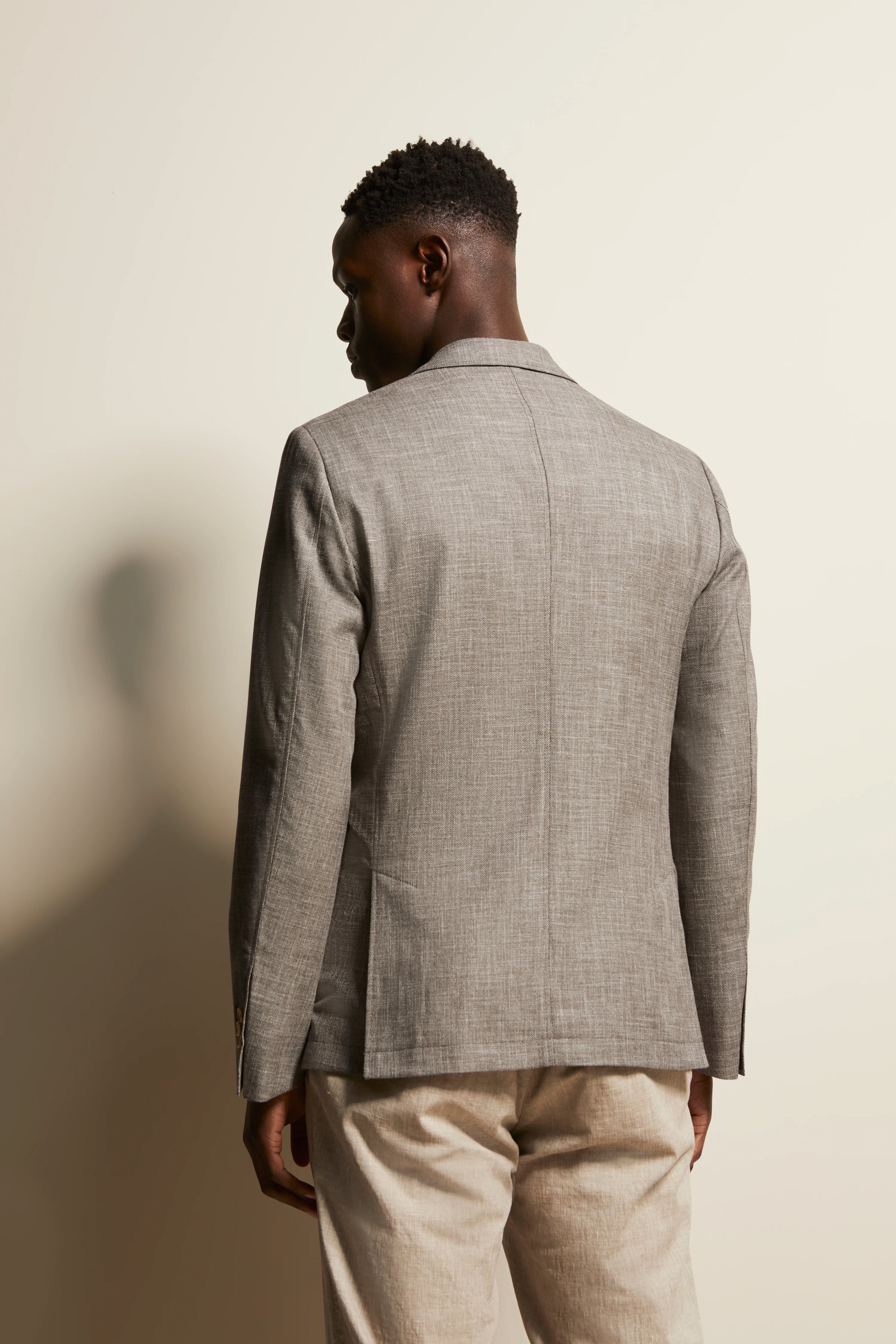 Grijze bugatti blazer, model van achteren, beige broek, ontspannen pose.