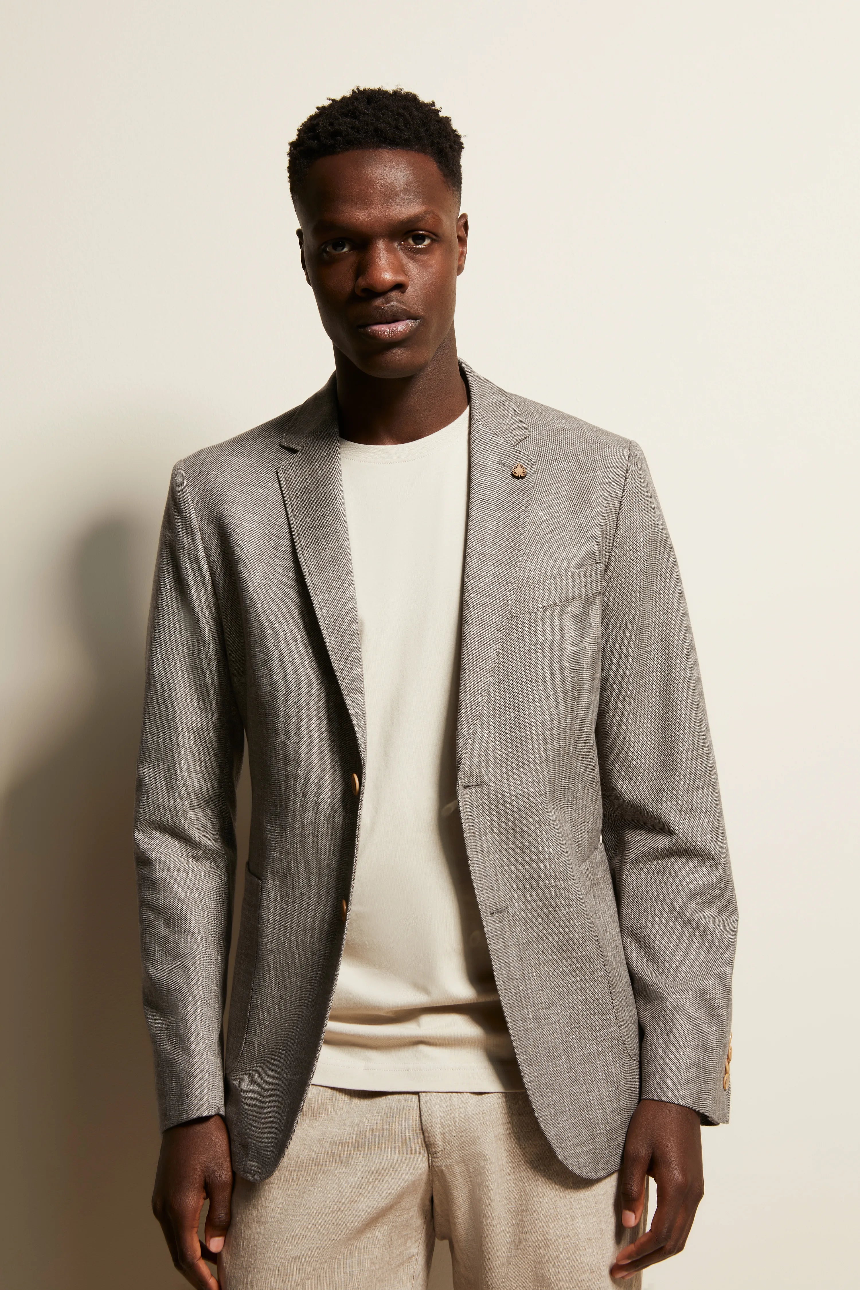 Grijs gemêleerde bugatti blazer, wit shirt, beige broek, model in ontspannen pose.