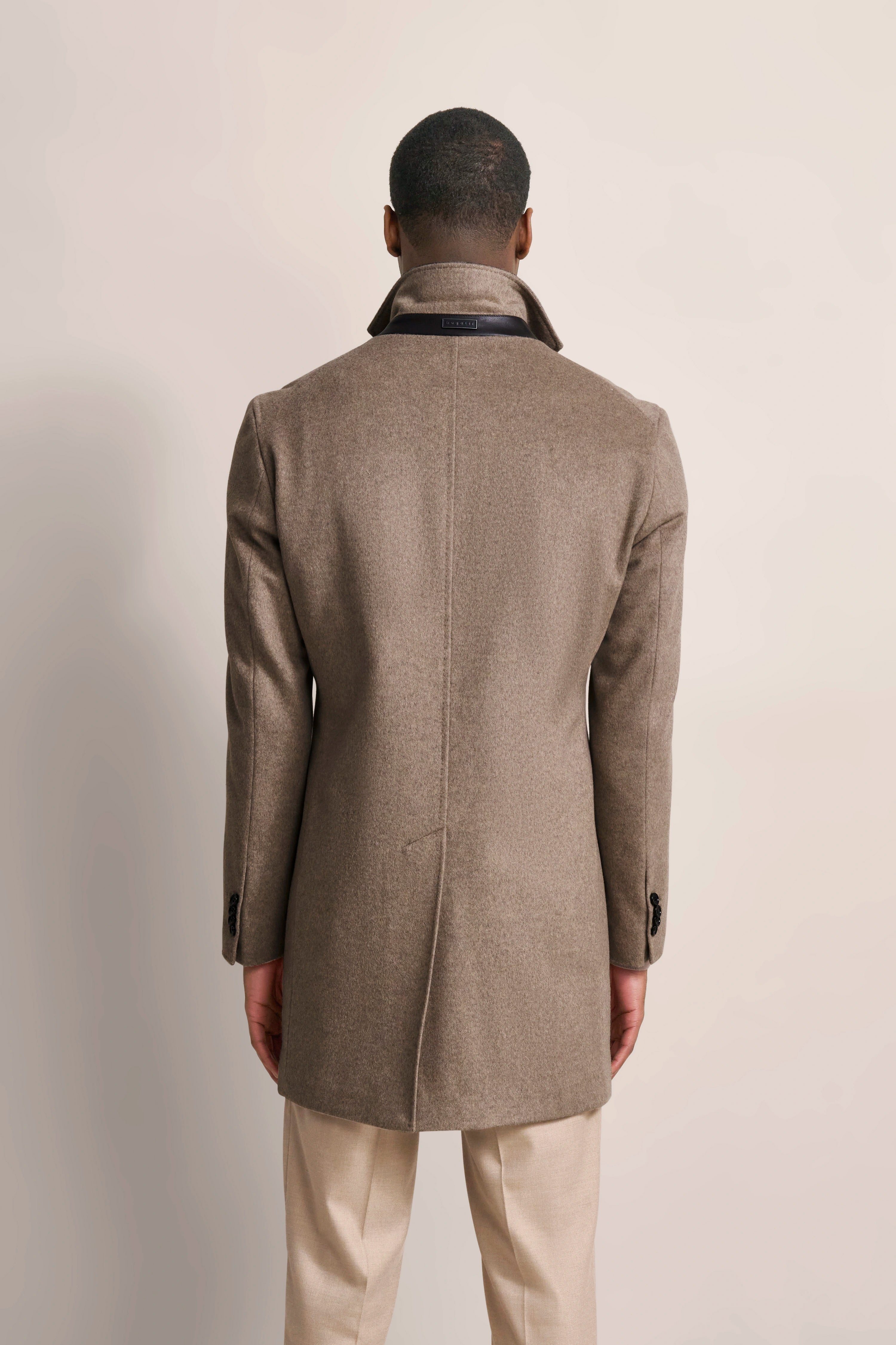 bugatti beige coat, back view, model in light pants, elegant pose.