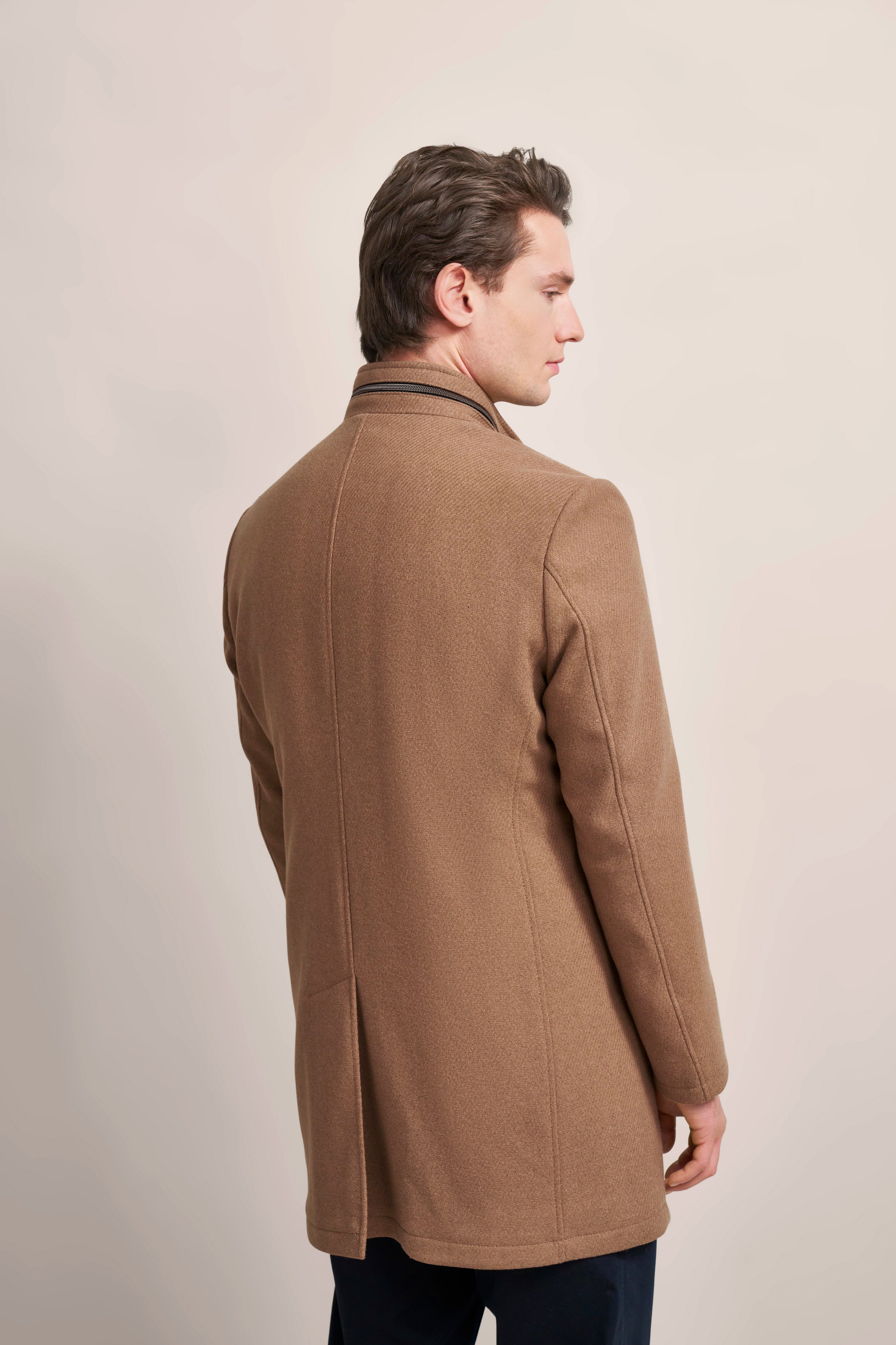 Brown bugatti coat, back view, over black pants, model looking sideways.