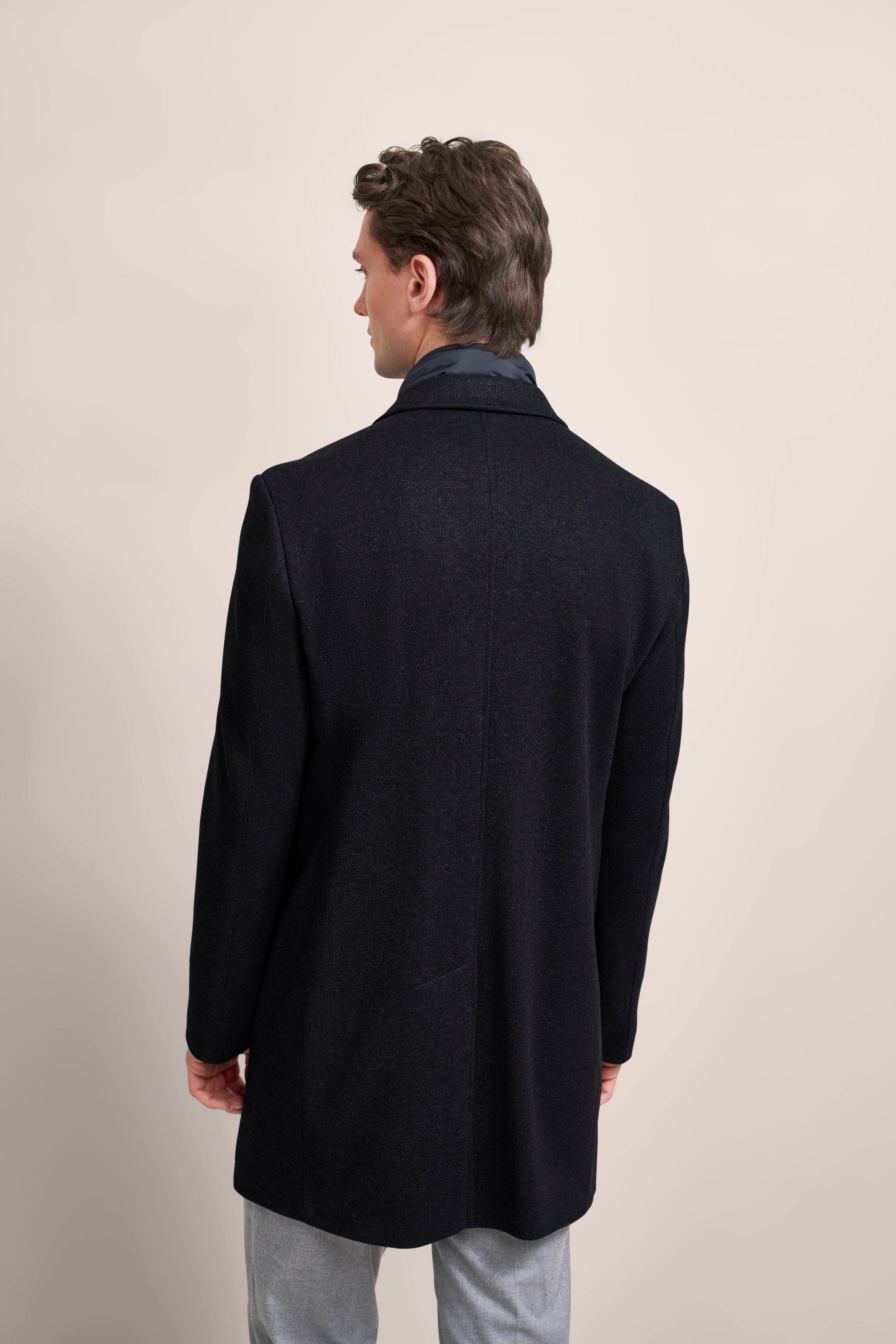 bugatti Mantel in Schwarz, Model von hinten, graue Hose, elegantes Outfit.