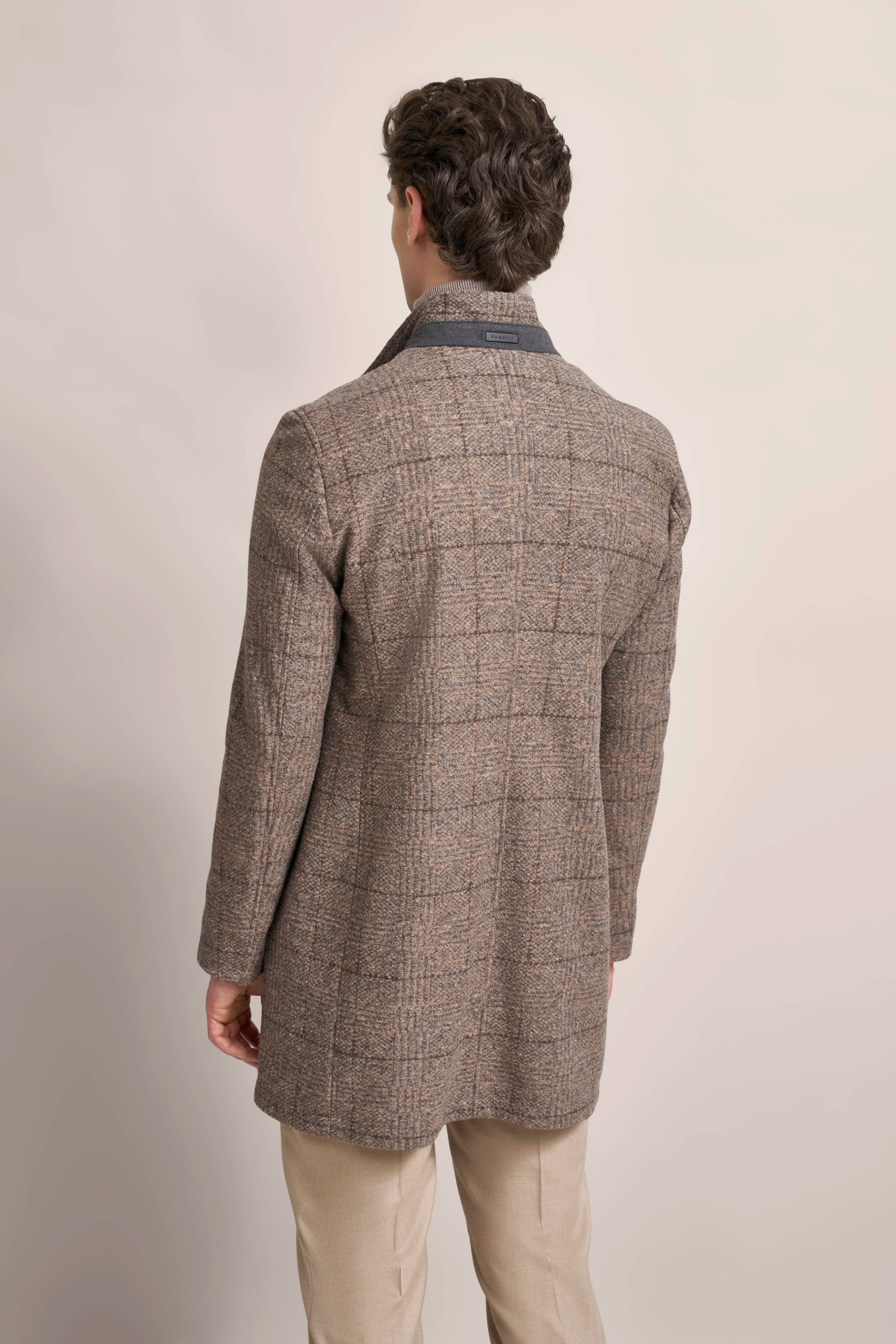 Rückansicht eines Models in kariertem bugatti Mantel, beige Hose, entspannte Pose.