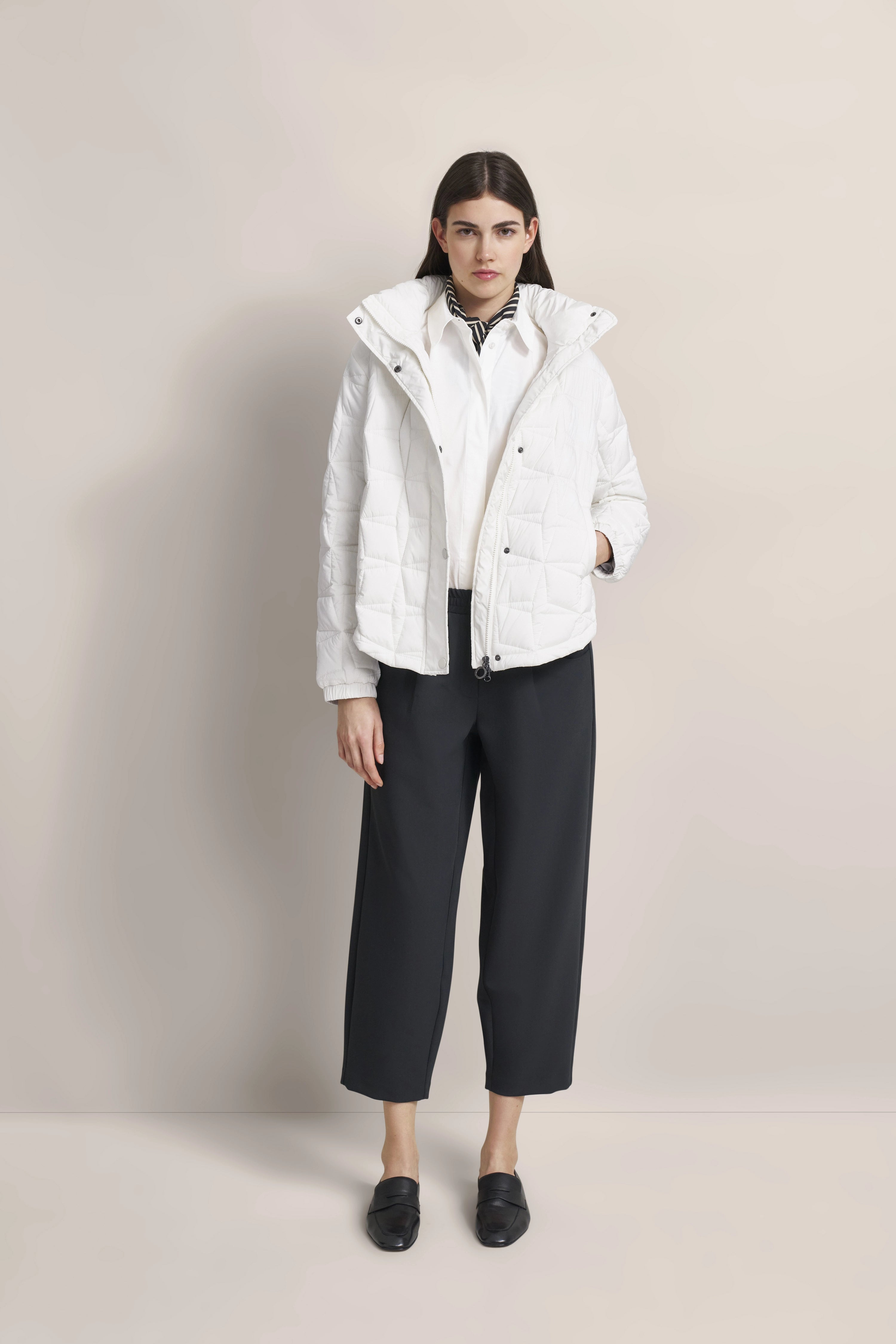 Model in white quilted jacket, white blouse, black pants, black scarf. Standing pose.
