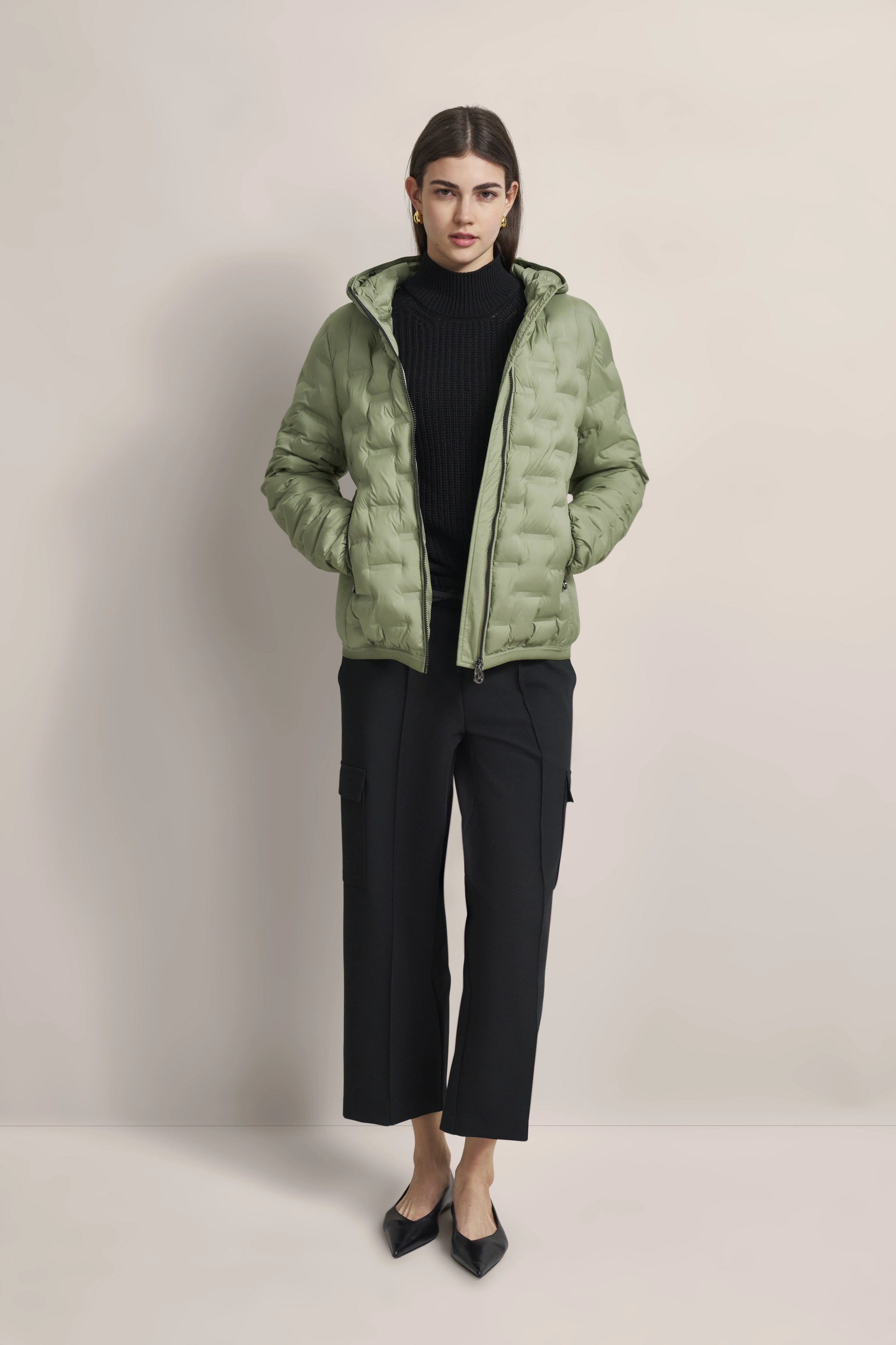 Model in green bugatti quilted coat, black turtleneck, black pants, casual pose.