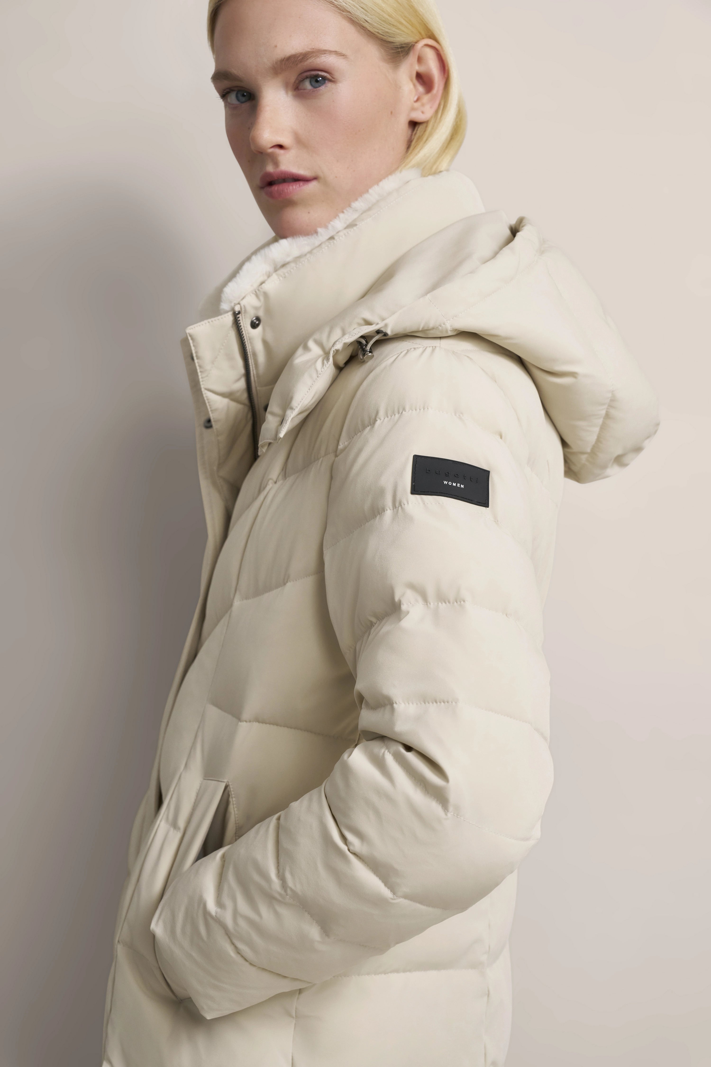 Model in cremefarbener bugatti Daunenjacke, seitliches Posing, eleganter Look.