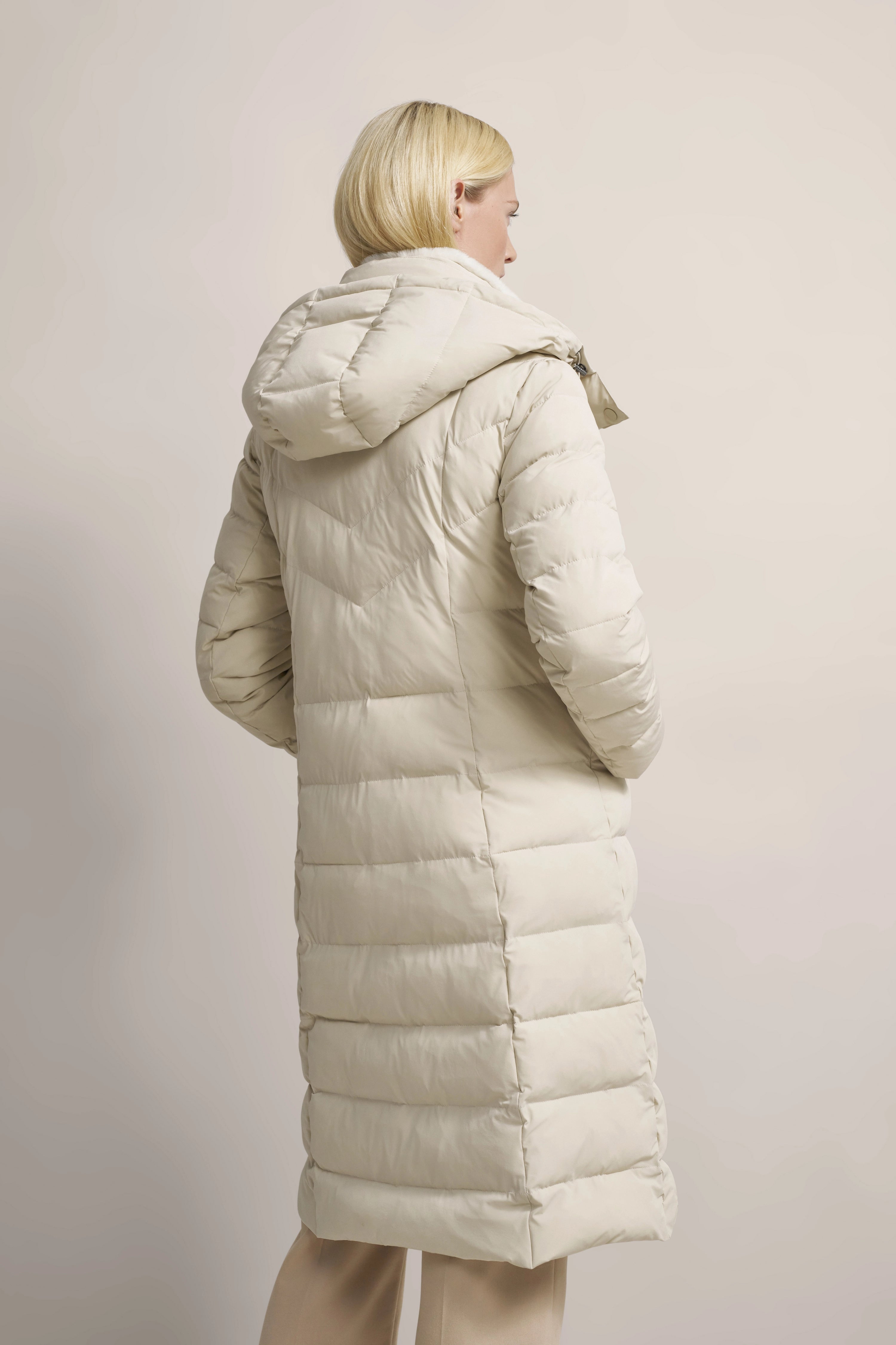 Damen-Model in beigem, gestepptem bugatti Mantel mit Kapuze, seitlich stehend.