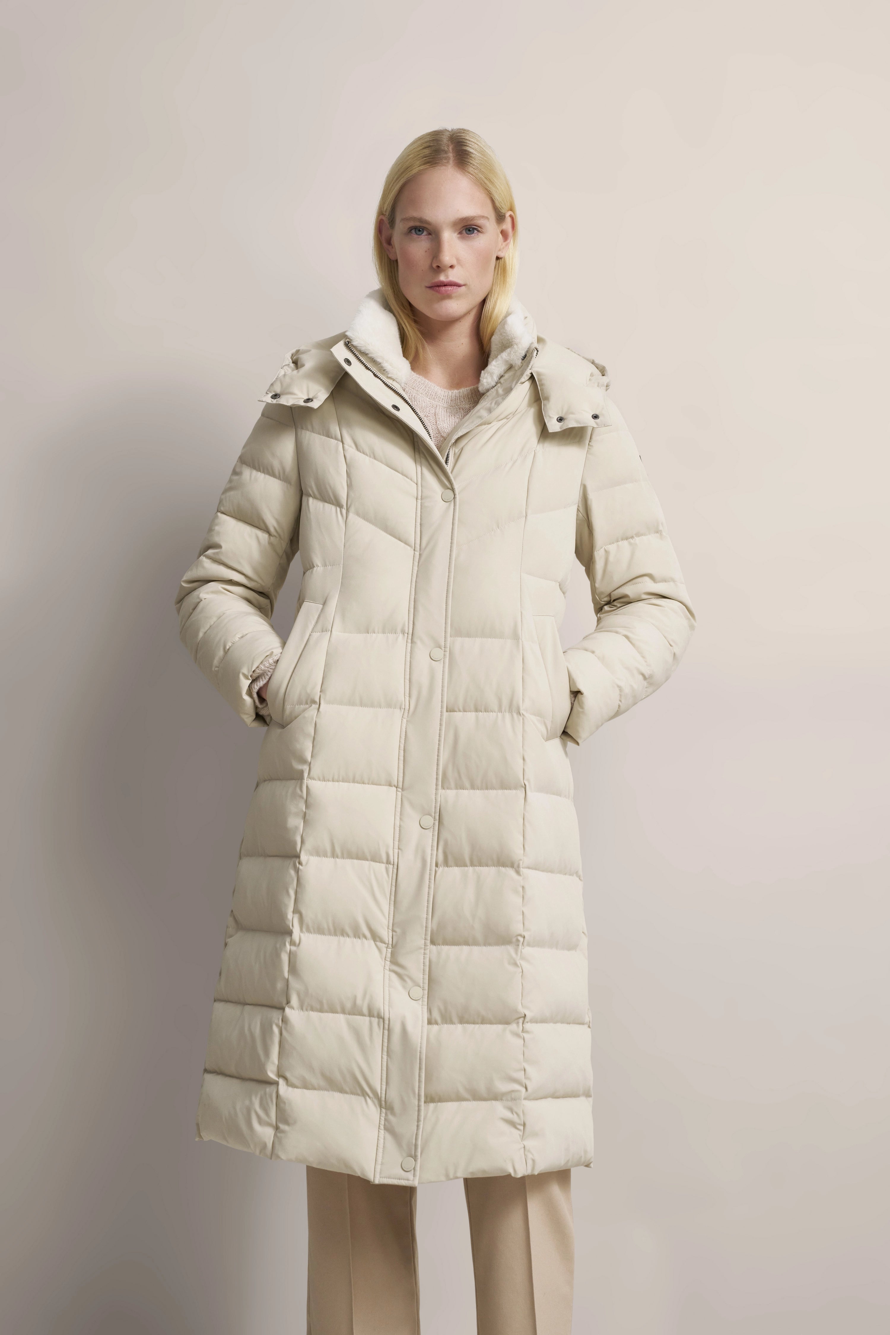 Langer beiger Steppmantel von bugatti, Modelbild, gerade Pose, Hände in den Taschen.