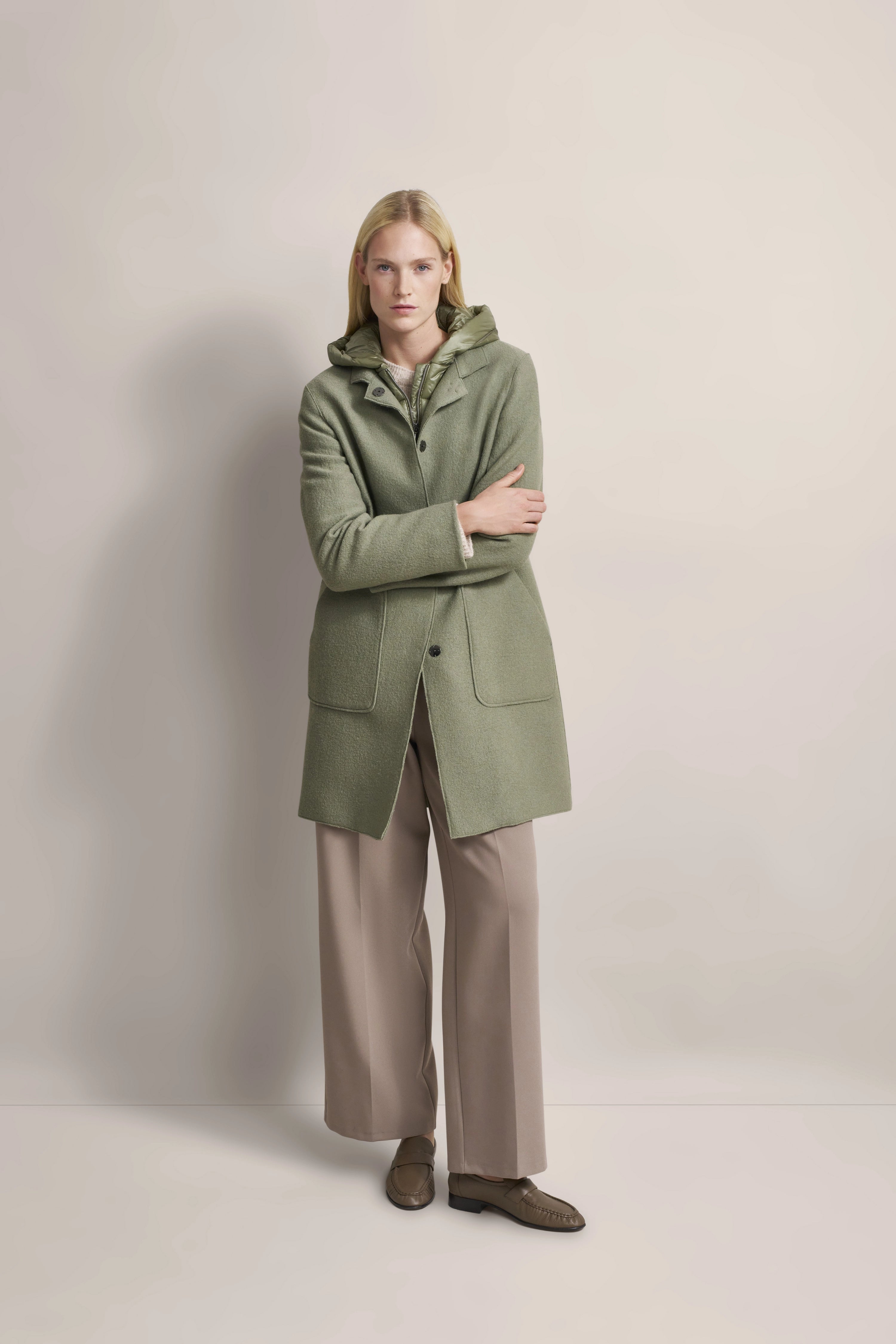 Grüner bugatti Mantel, beige Hose, legeres Modelbild mit verschränkten Armen.