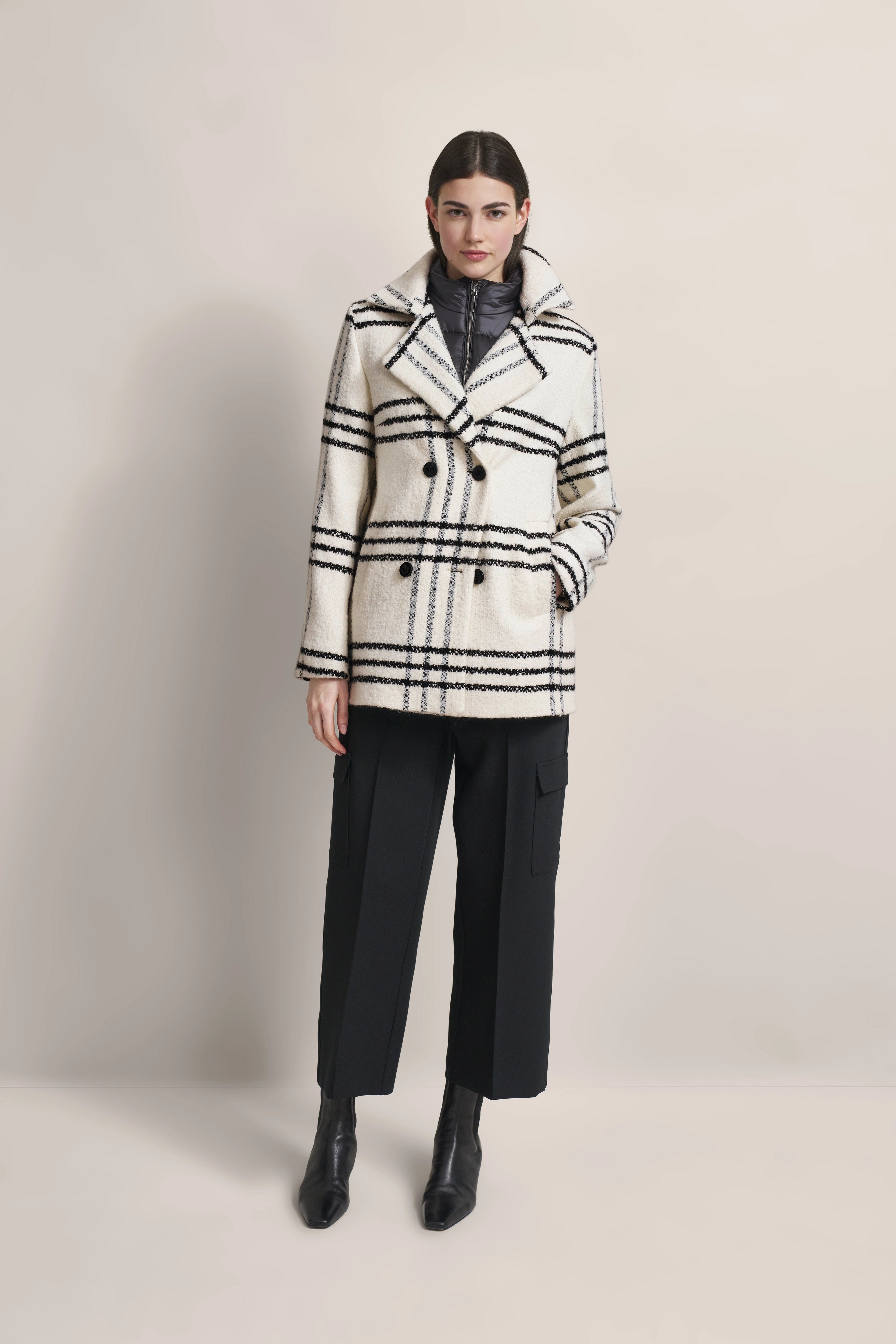 Model in cremefarbenem karierter bugatti-Mantel, schwarzer Hose und Stiefeln, entspanntes Posing.