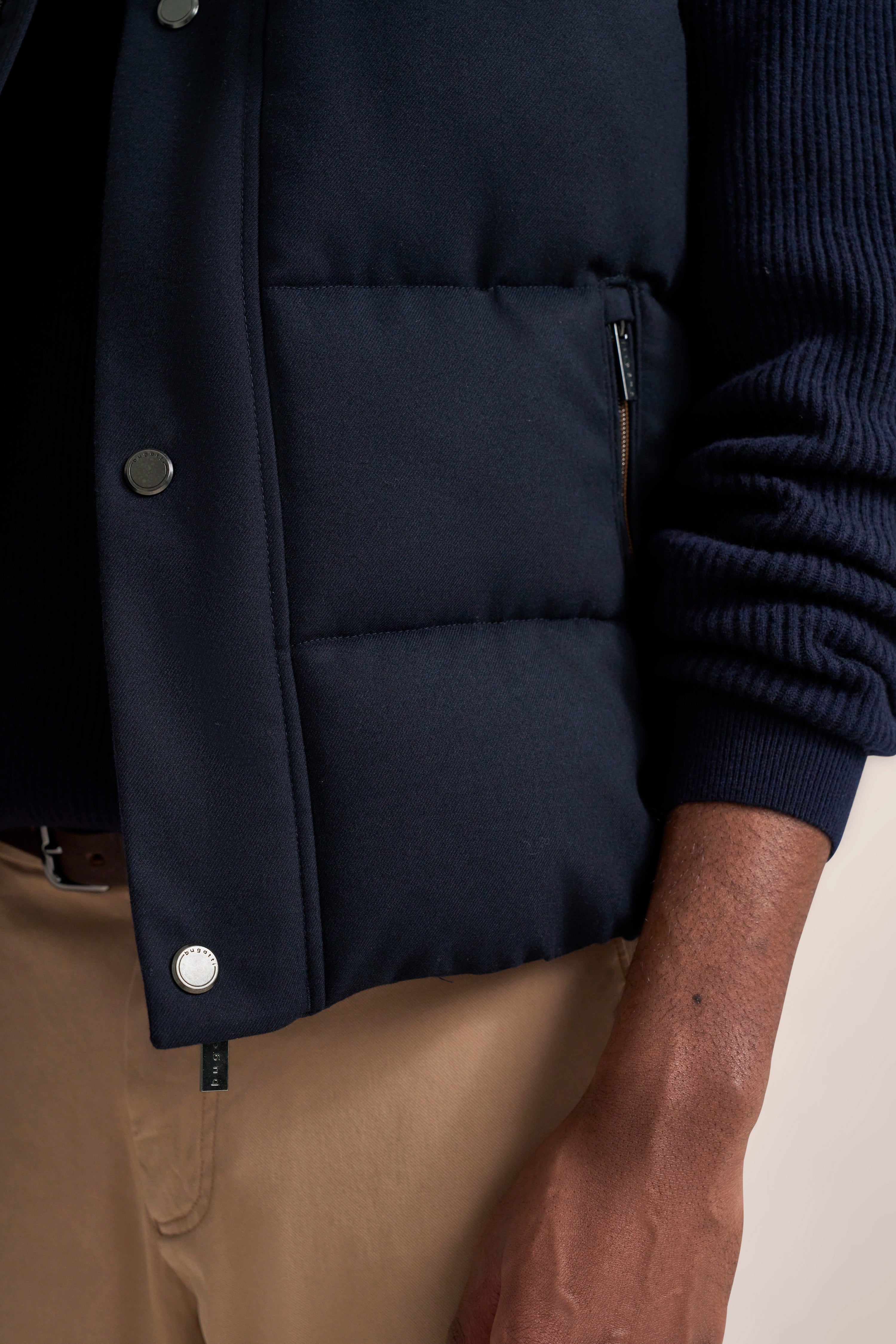 Dark blue quilted vest and sweater, beige pants, casual detail shot.
