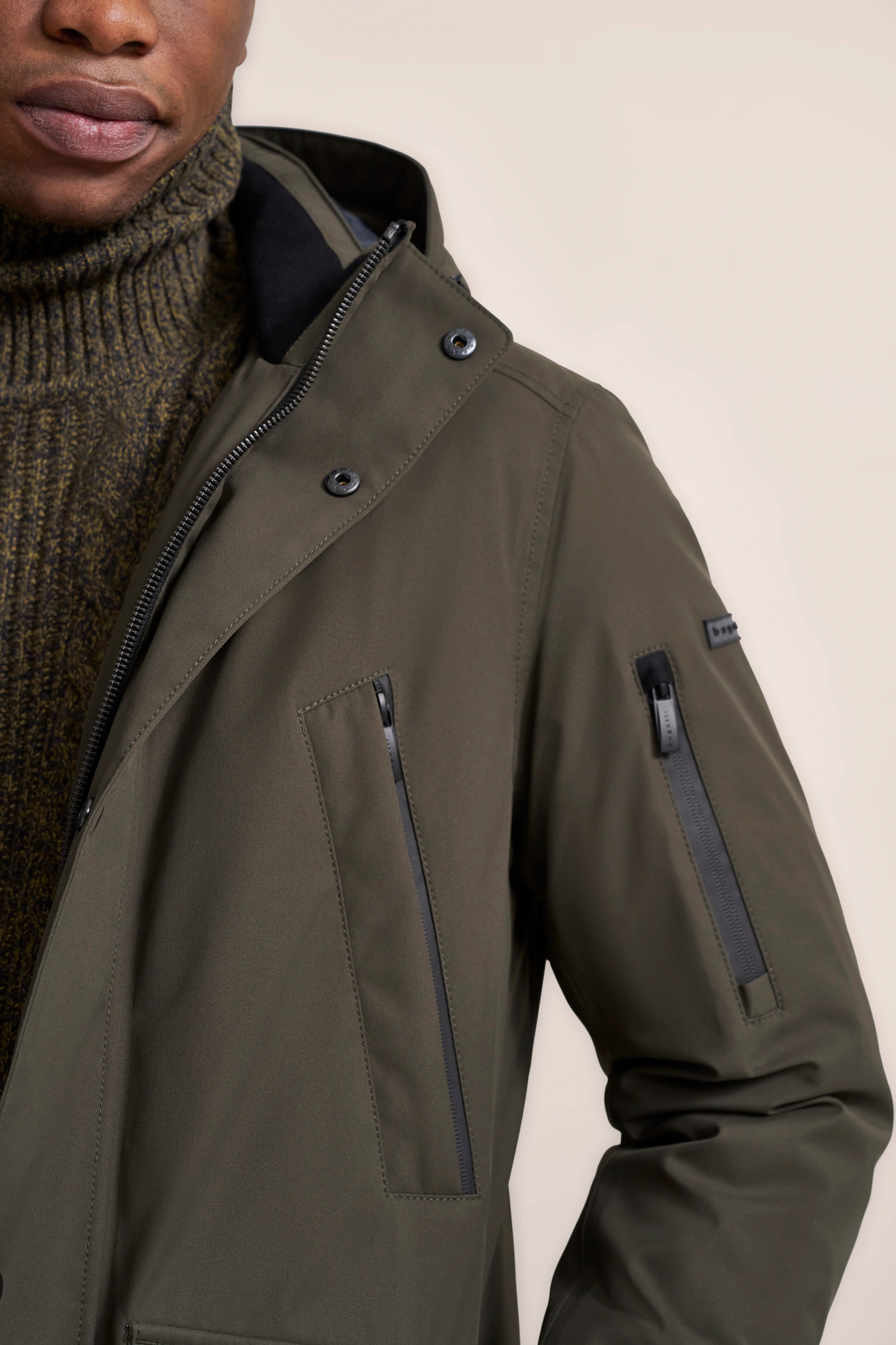 Olivgrüne bugatti Jacke mit Reißverschlusstaschen, kombiniert mit olivfarbenem Rollkragenpullover, Modelbild.