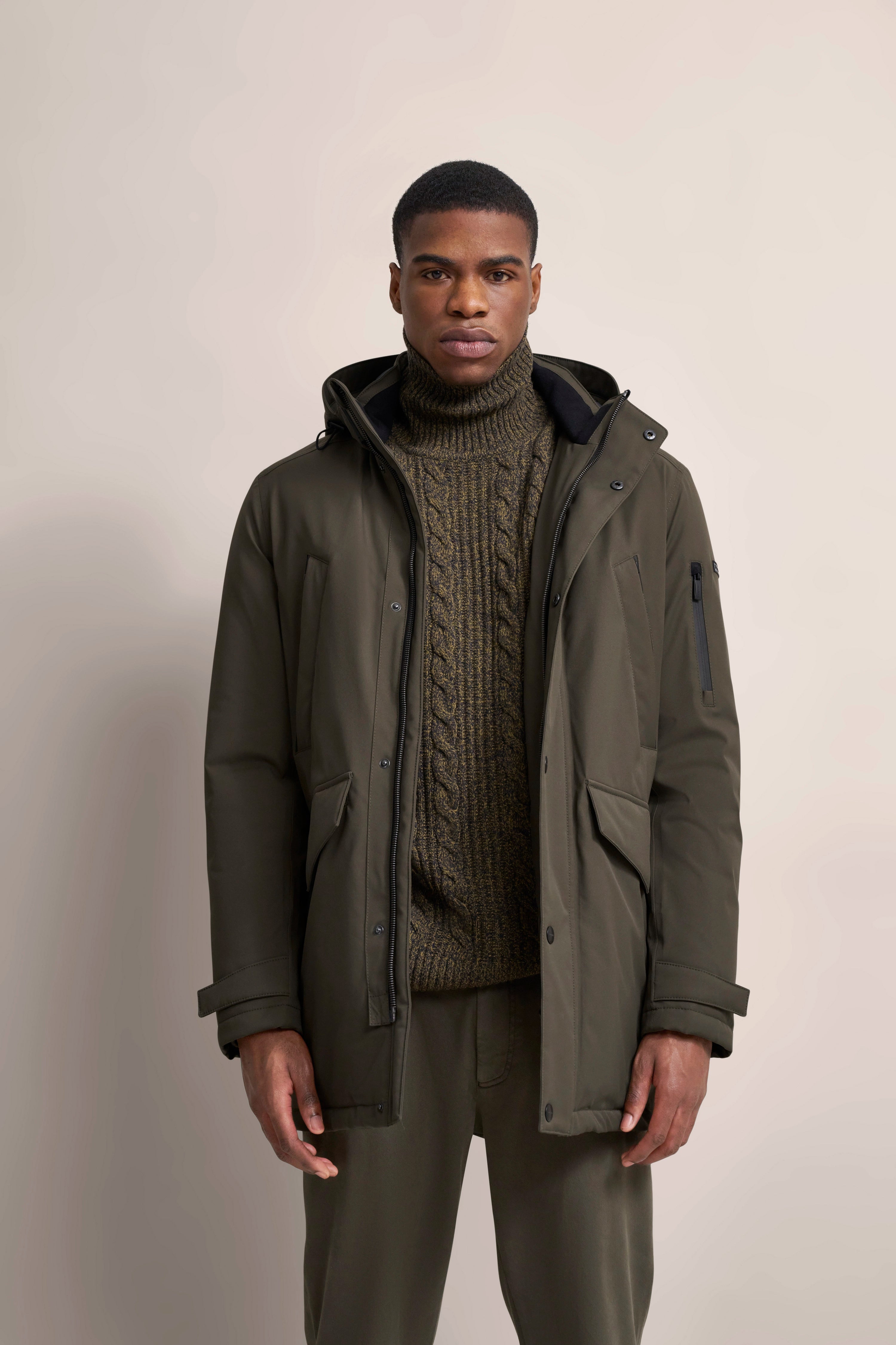 Model in olivgrüner bugatti Jacke und Strickpullover, leger stehend.