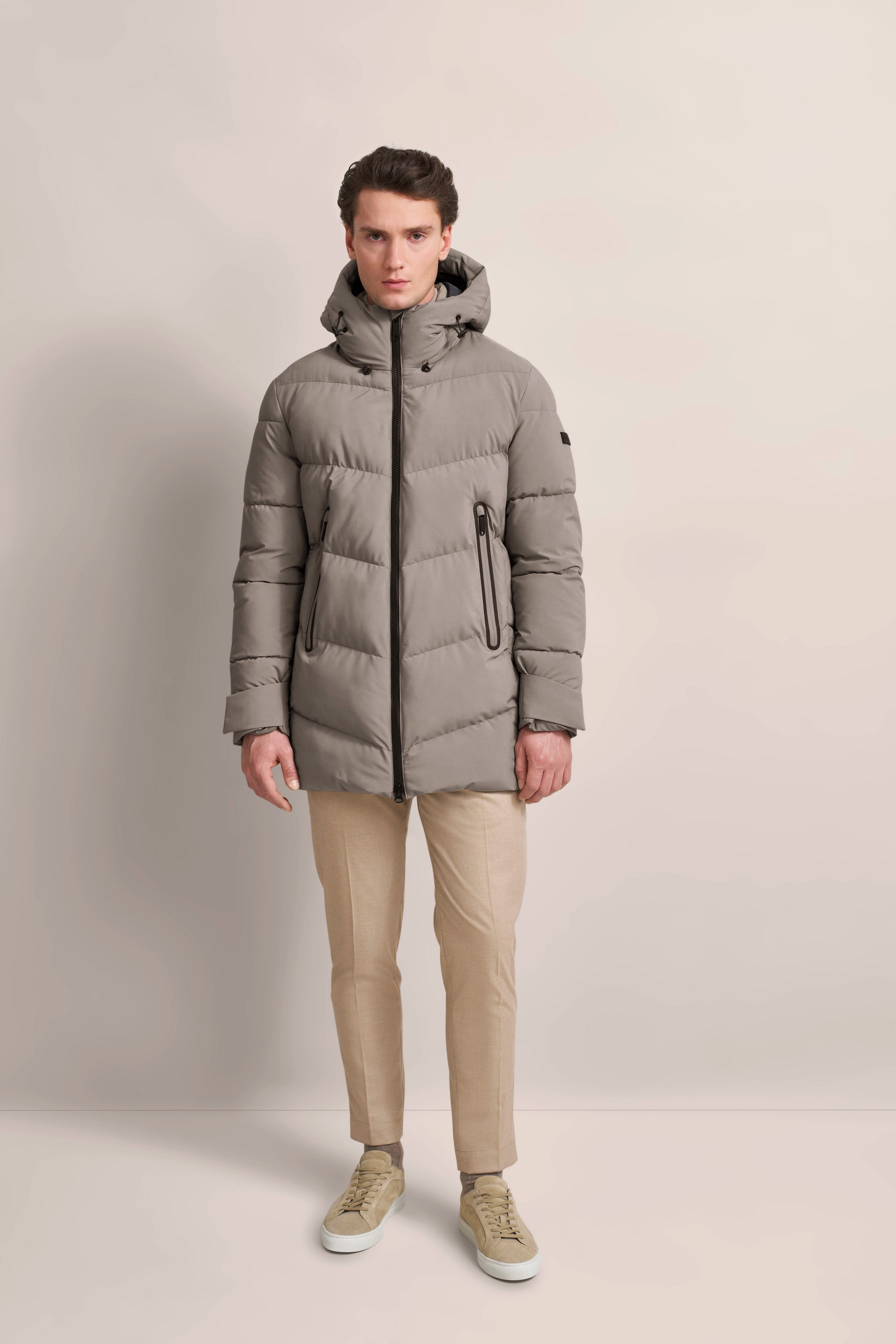 Modelbild: Graue bugatti Steppjacke, beige Hose, helle Sneakers, frontales Posing.